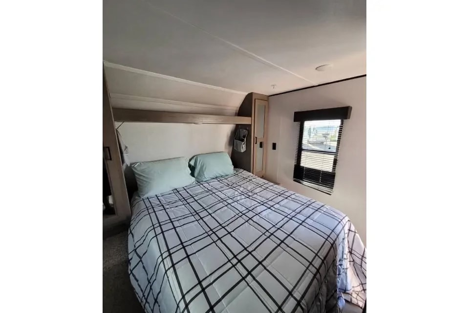 RV rental bedroom featuring a queen bed with plaid comforter, window, and storage.. Keystone RV Hideout 2021
