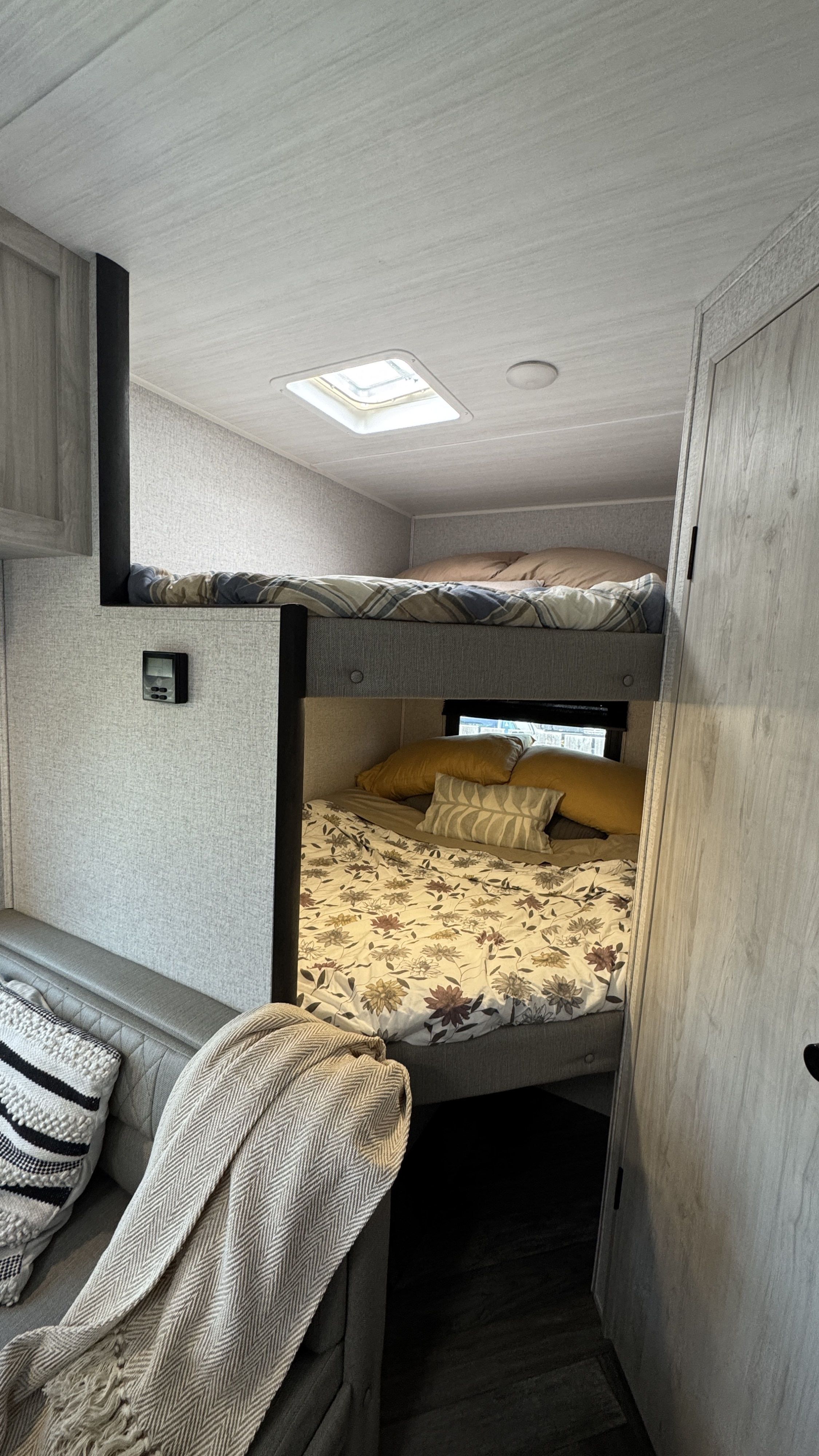 Inside this RV rental, a cozy bunkhouse with an upper plaid-covered bed and a lower floral bed. A sofa is in the foreground.. East to West Della Terra LE 2023
