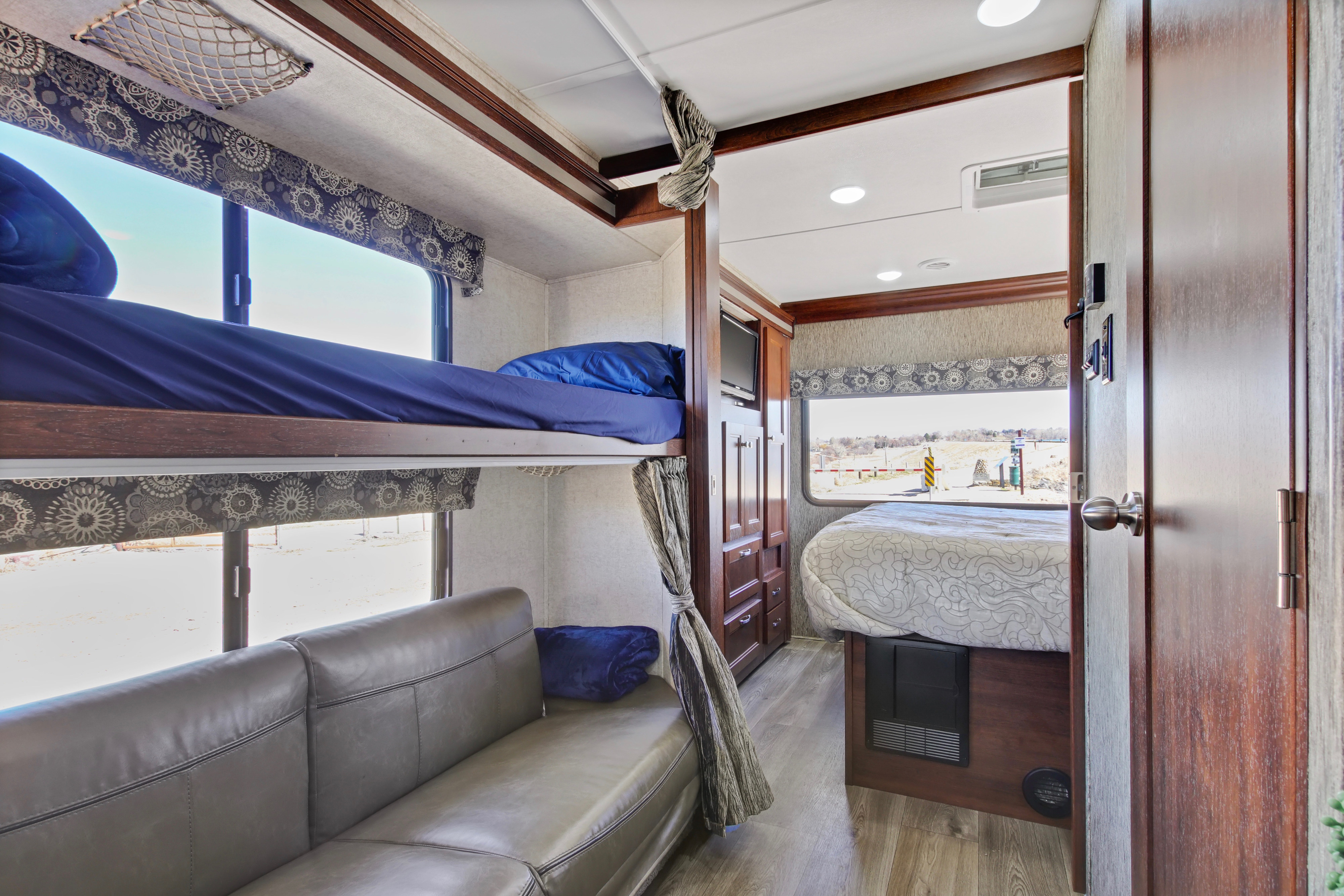 Inside an RV rental: bunk beds, a gray sofa, and a queen bed in the master area, all with wood finishes.. Forest River Sunseeker 2016