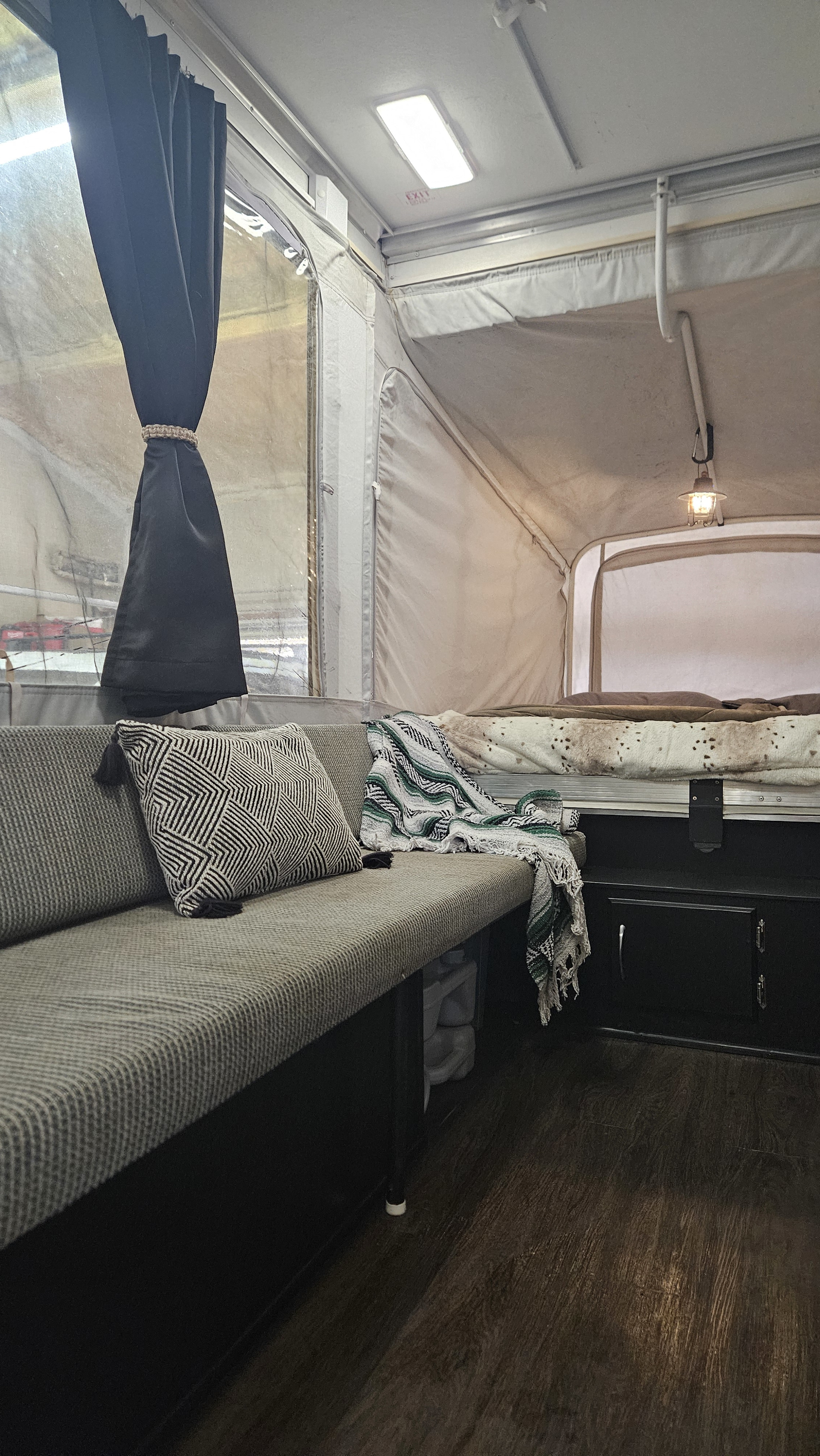 Inside an rv rental: a cozy grey sofa, patterned pillow, wood flooring, and a comfortable pop-out bed area.. Fleetwood Neon 2006