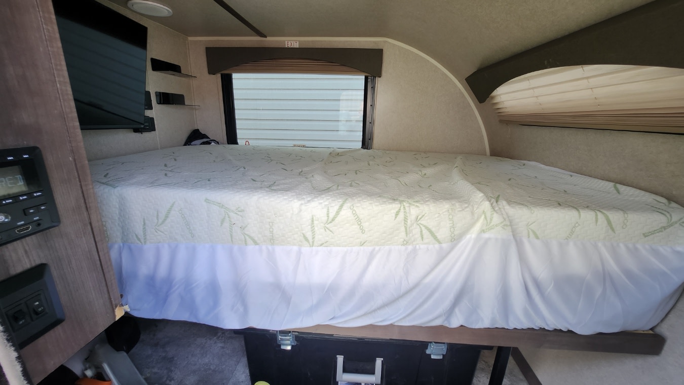 Inside an RV rental: a comfy sleeping area with a Bamboo mattress, bed skirt, window, and TV for a relaxing trip.. Sunset Park RV SunRay 2023