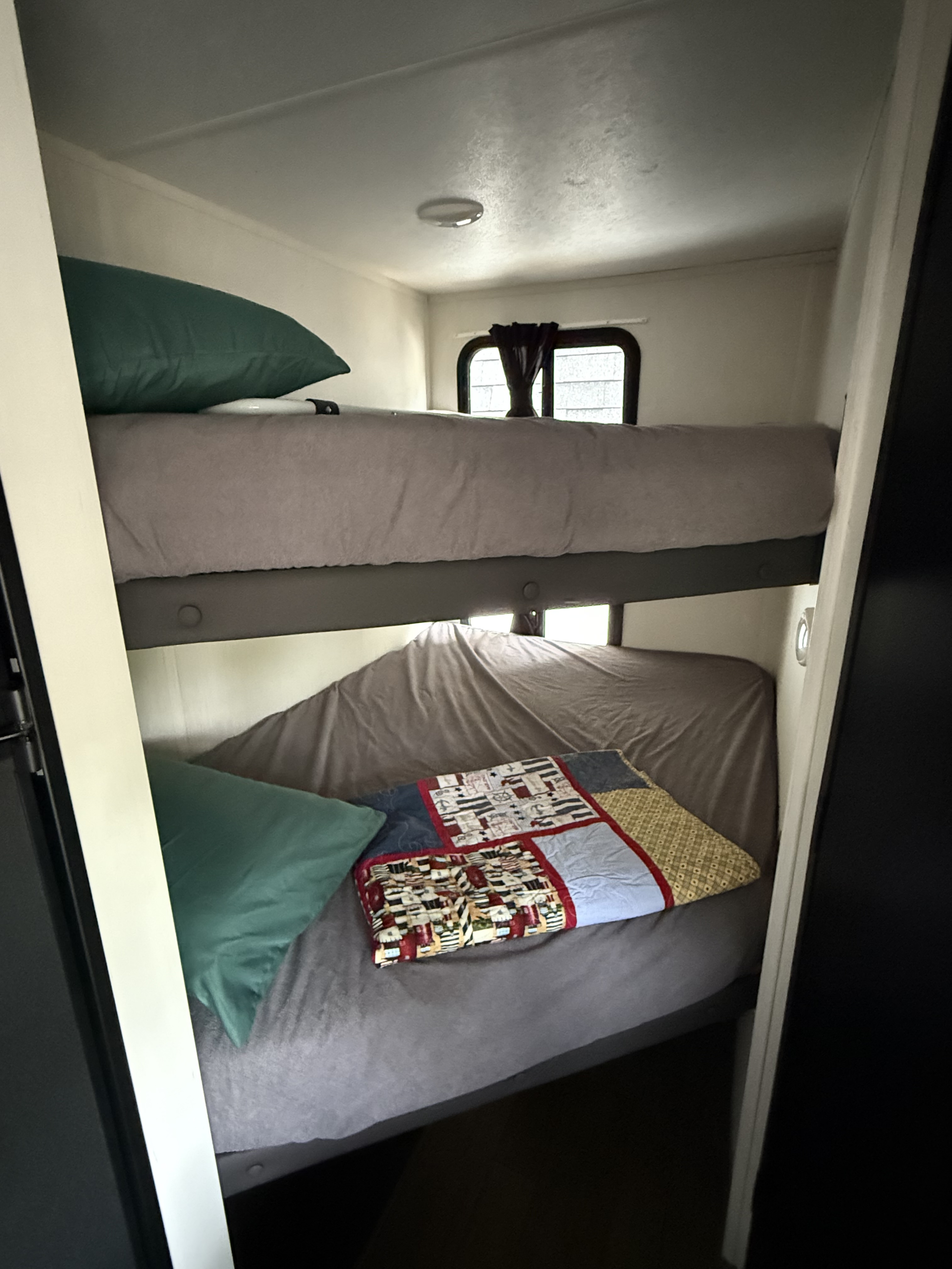 RV rental interior: two cozy bunk beds with grey bedding and green pillows, featuring a colorful quilt on the bottom.. Forest River Wildcat 2022