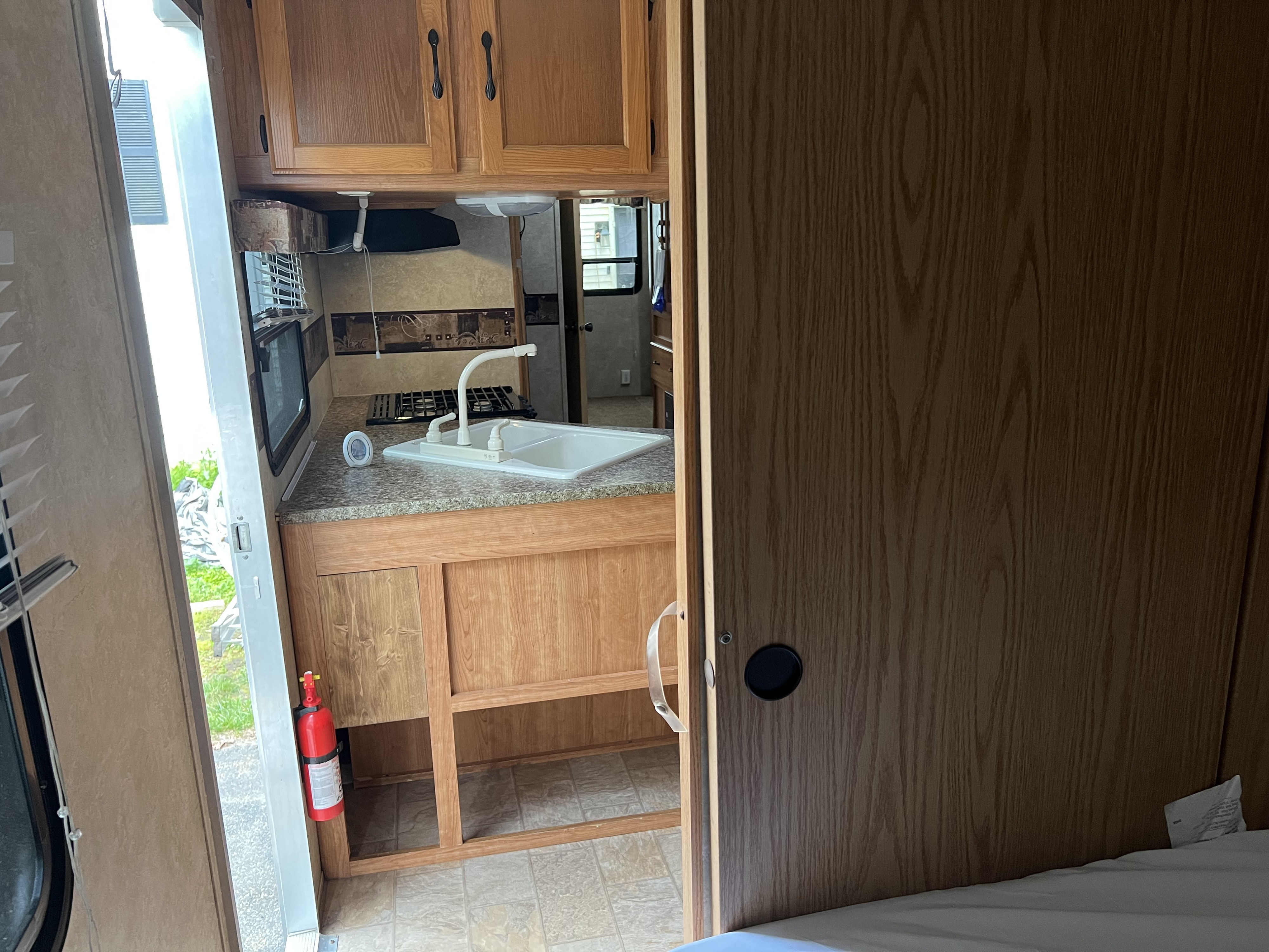 This RV rental's compact kitchen features a sink, stovetop, storage, and a visible fire extinguisher for safety.. Keystone RV Sprinter Select 2010