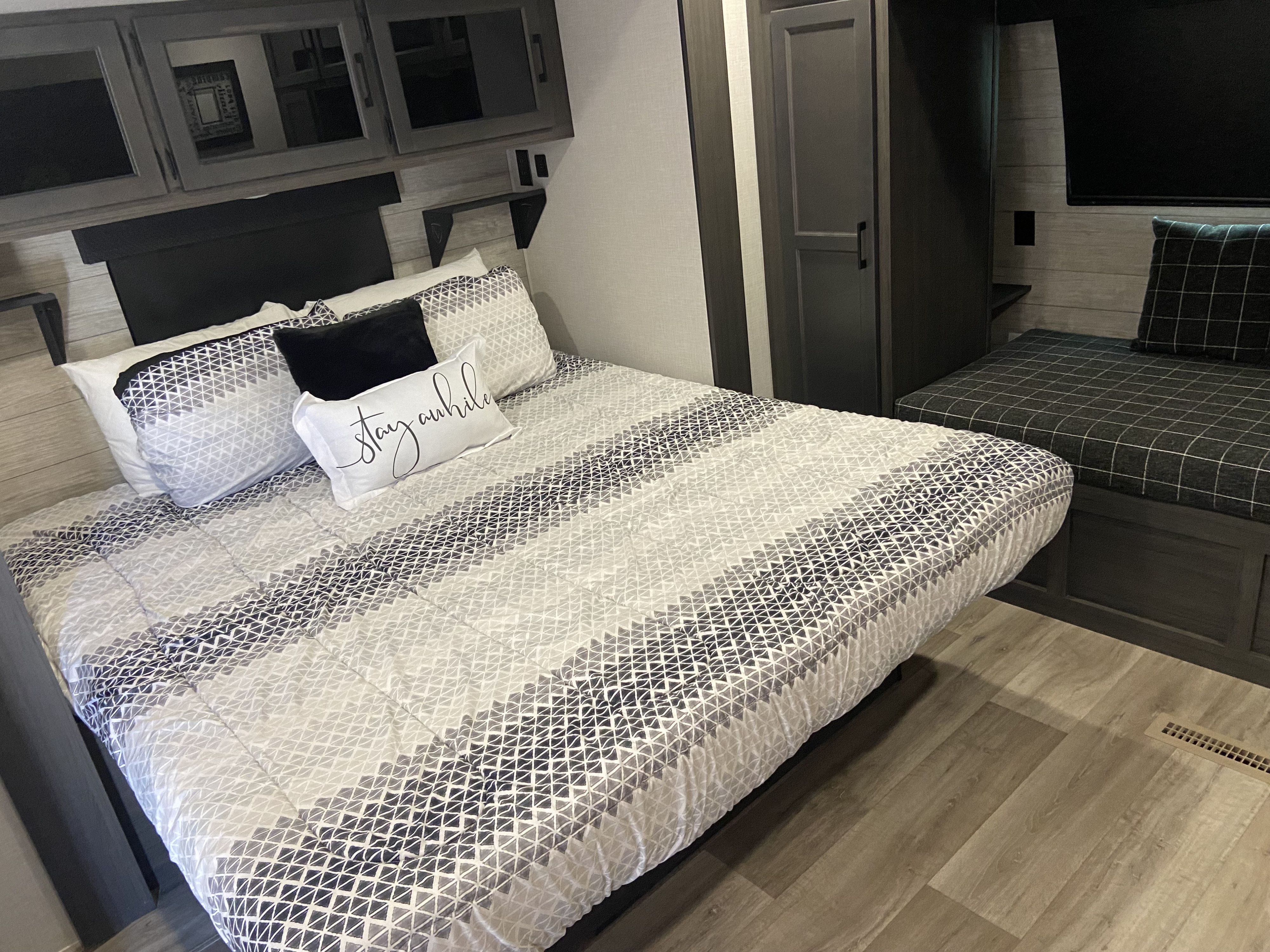 Cozy RV rental bedroom with a modern bed featuring geometric bedding, overhead cabinets, and a seating nook.. Venture Rv Sporttrek 2026