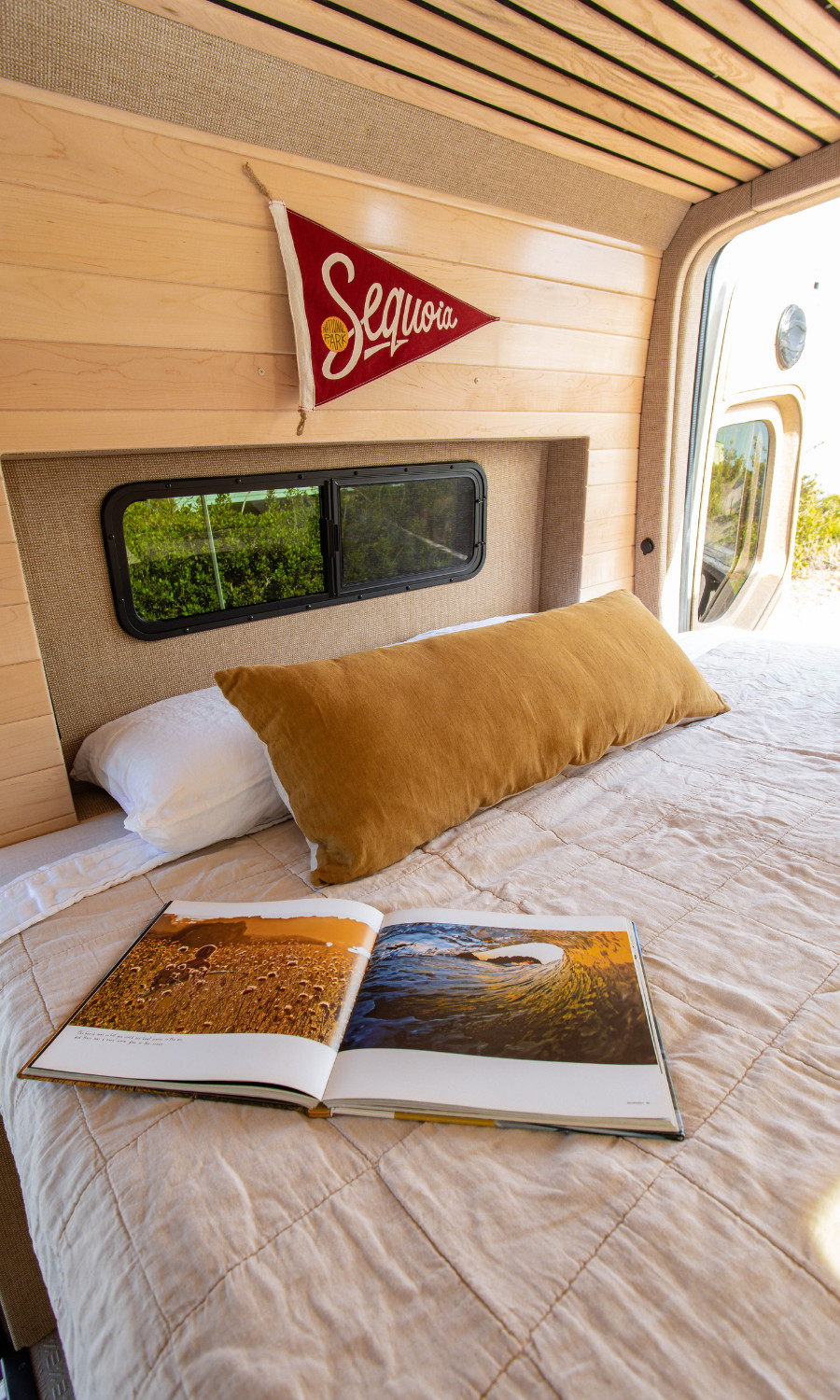 Relax in your RV rental's comfy bed! This camper van boasts wood paneling, a view window, and reading space.. Mercedes-Benz Sprinter 2025