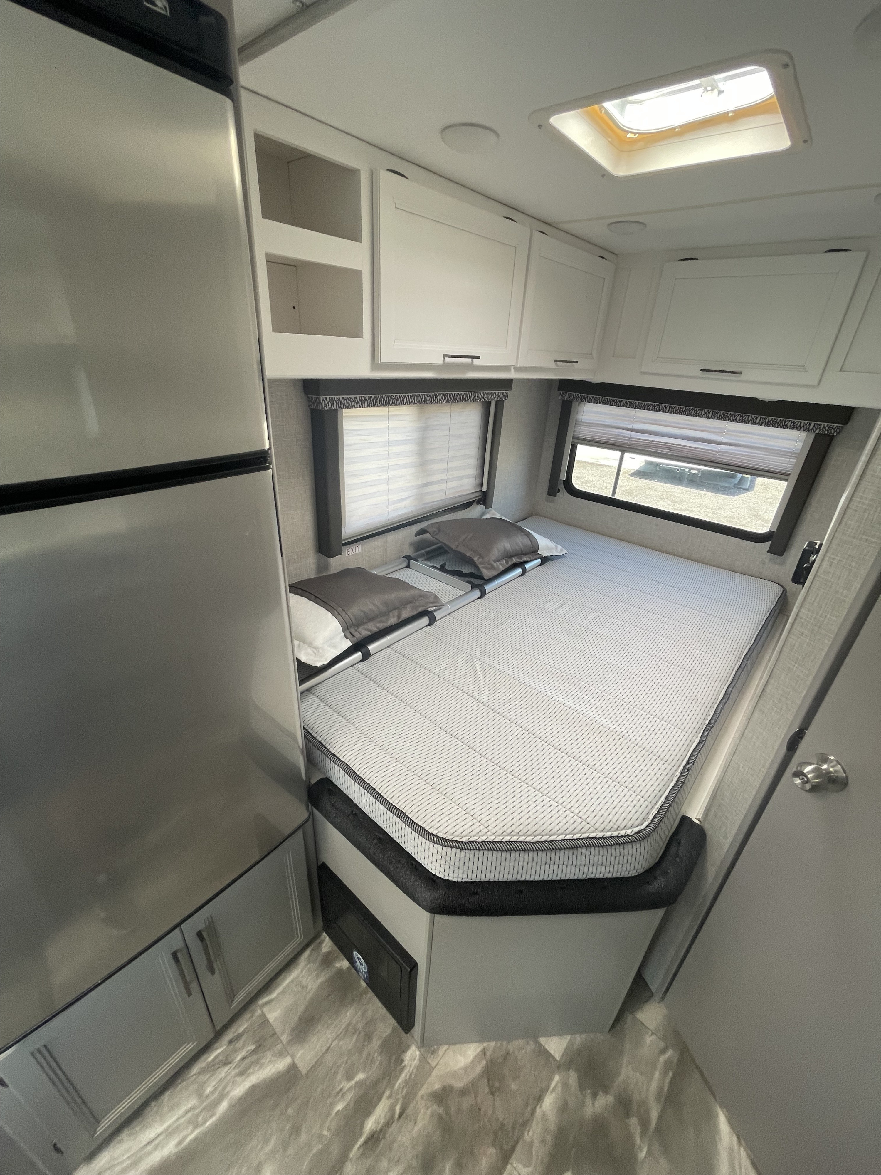 Clean and bright RV rental interior featuring a comfortable bed, large refrigerator, overhead storage, and windows.. Thor Quantum LC 2024