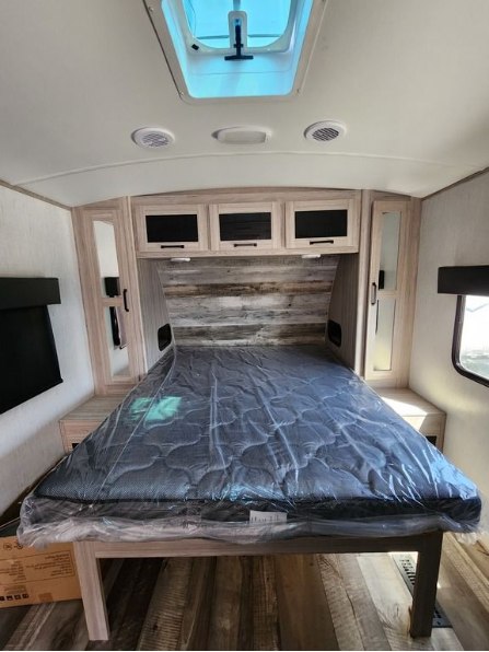 Clean RV rental bedroom featuring a new mattress in plastic, overhead storage, and ceiling skylight. Ready for your trip!. Heartland RVs Sundance Ultra Lite 2023