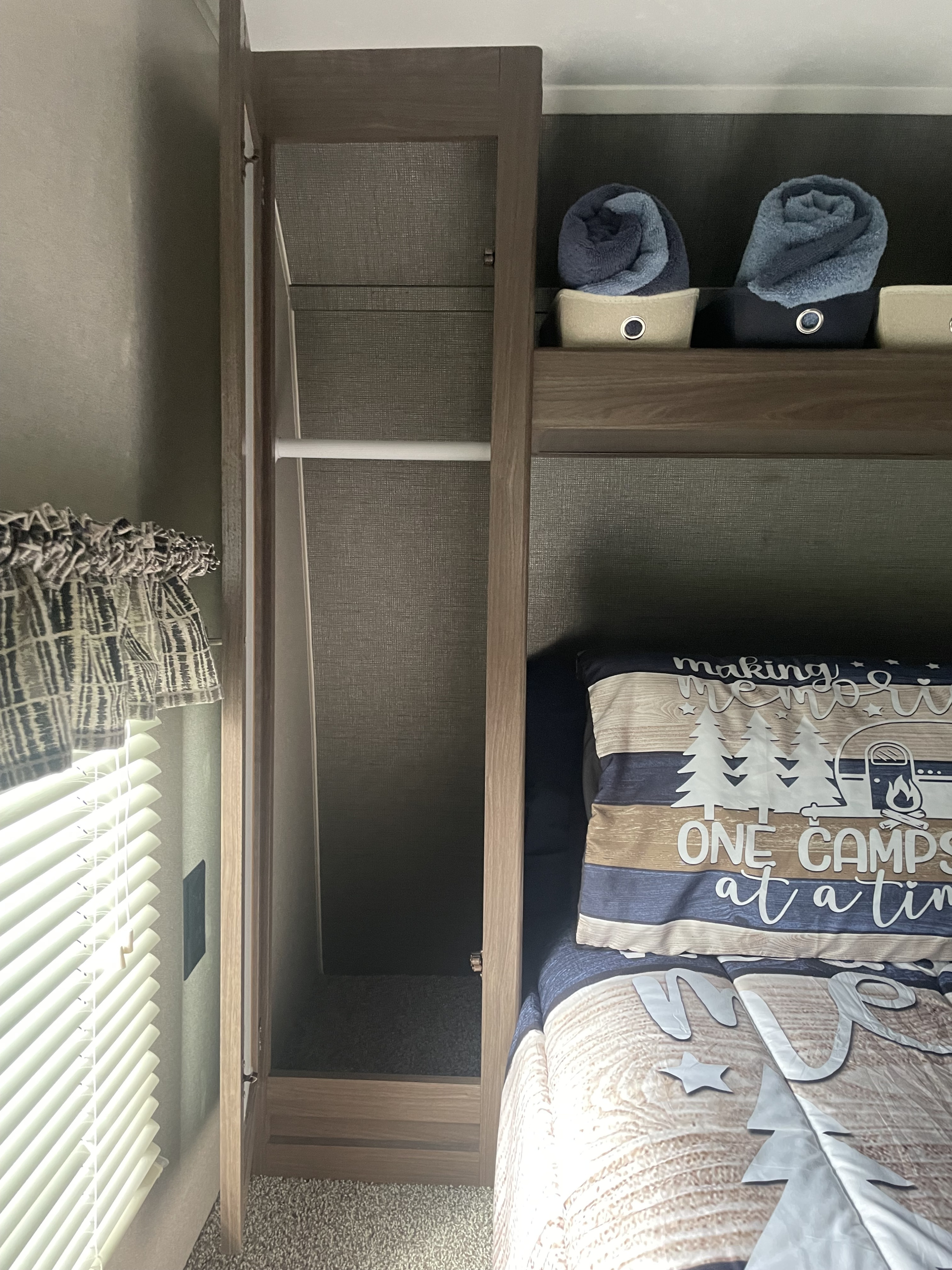 Compact RV rental bedroom with an open wardrobe, storage shelves, and a cozy bed, optimizing space for travel.. Keystone RV Hideout LHS 2018