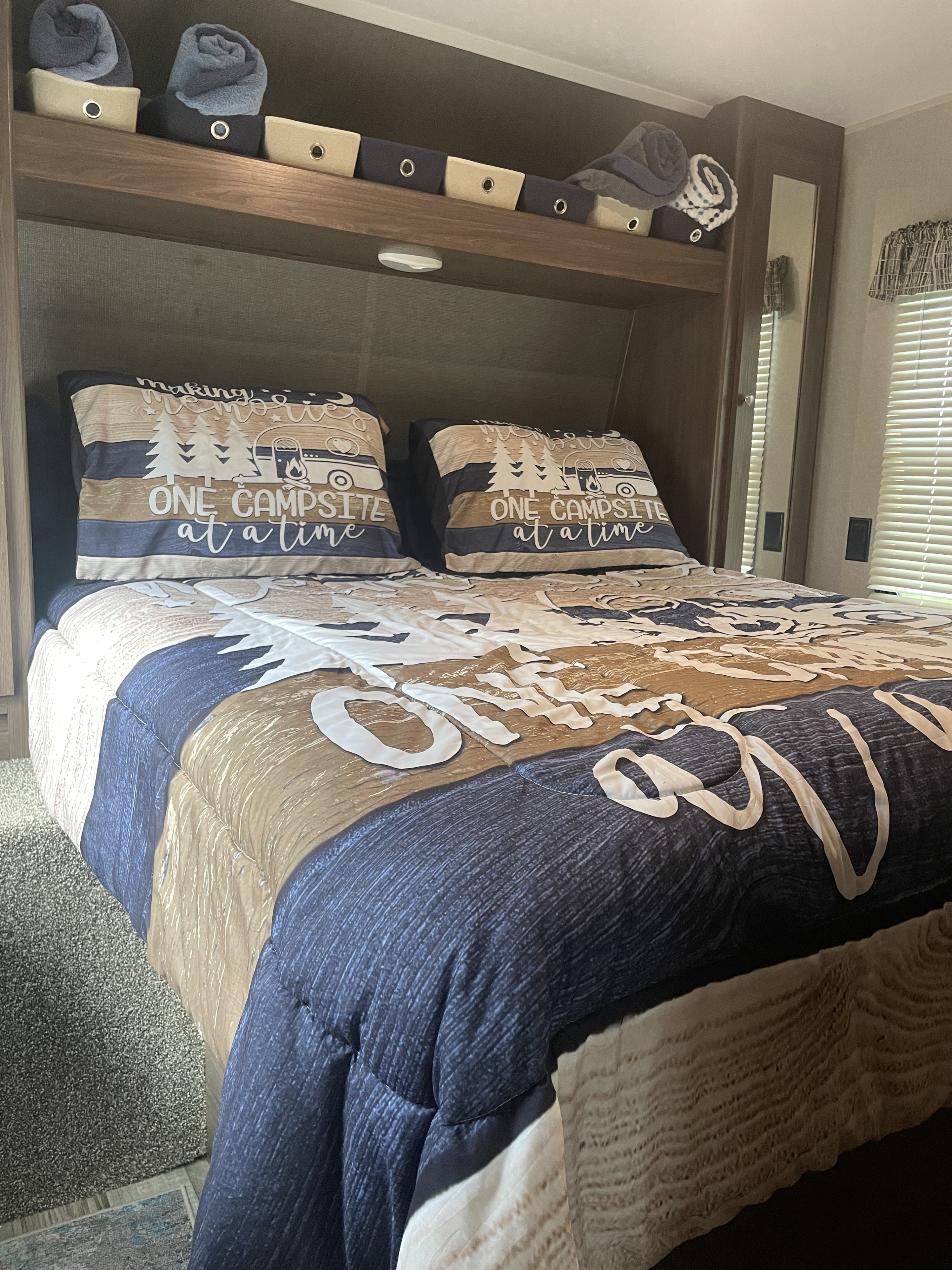 Cozy RV rental bedroom with "ONE CAMPSITE" themed bedding, overhead bins storing towels, and window blinds.. Keystone RV Hideout LHS 2018