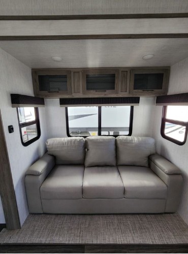Cozy RV rental interior with a light gray sofa, overhead cabinets, and windows.. Heartland RVs Elkridge 2022
