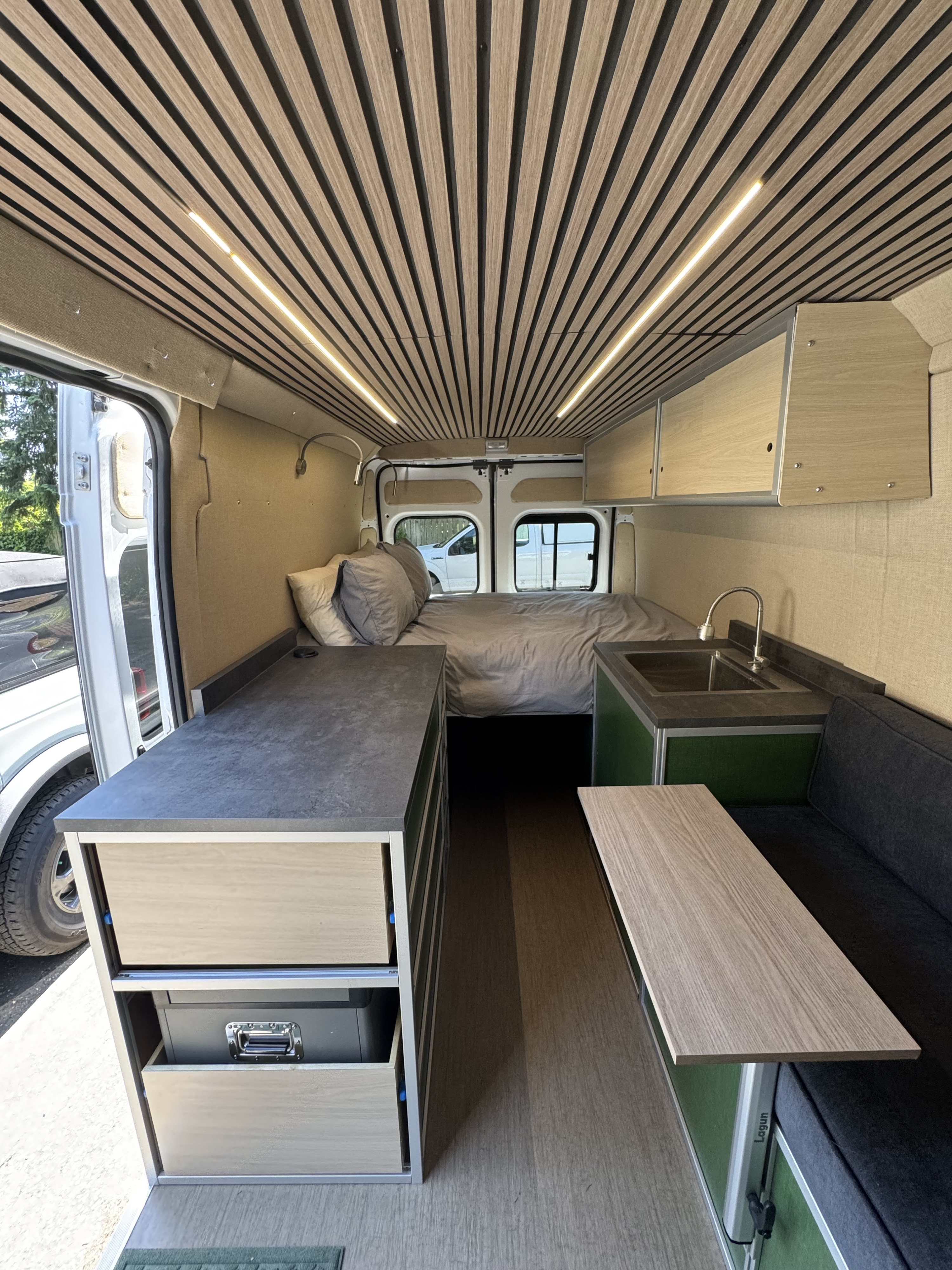 Step inside this modern RV rental: a compact living space with a bed, kitchen, custom storage, and stylish wood accents.. Dodge B Van 2023