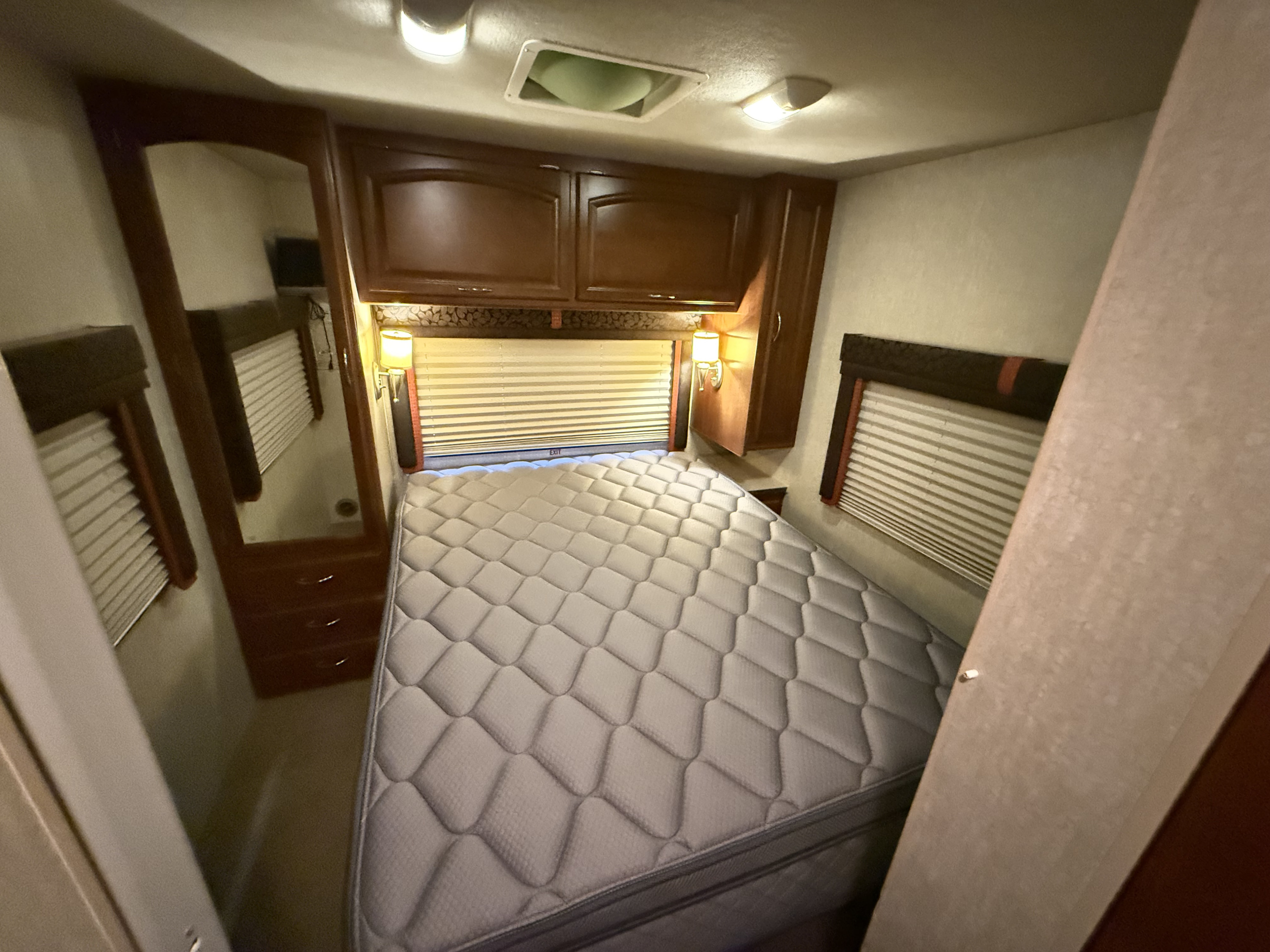 Cozy RV rental bedroom with a large mattress, overhead cabinets, and window blinds, designed for comfortable travel.. Jamboree GT 2008