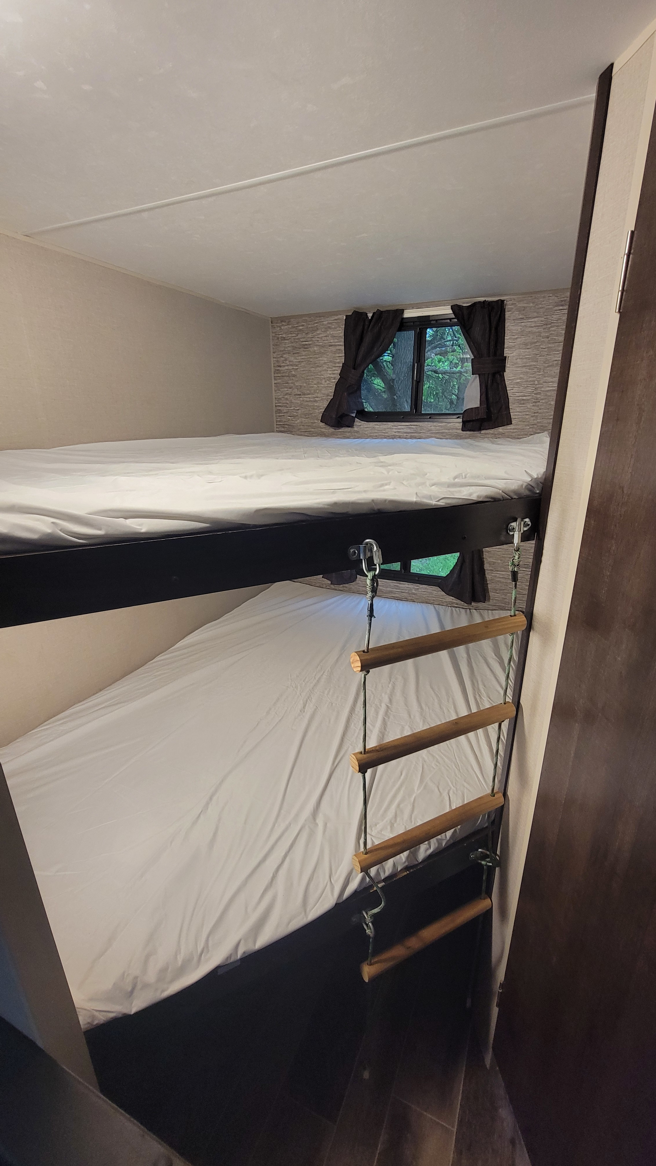 Cozy RV rental sleeping area featuring bunk beds with white sheets and a rope ladder. A window overlooks green trees.. KZ 260bh 2019