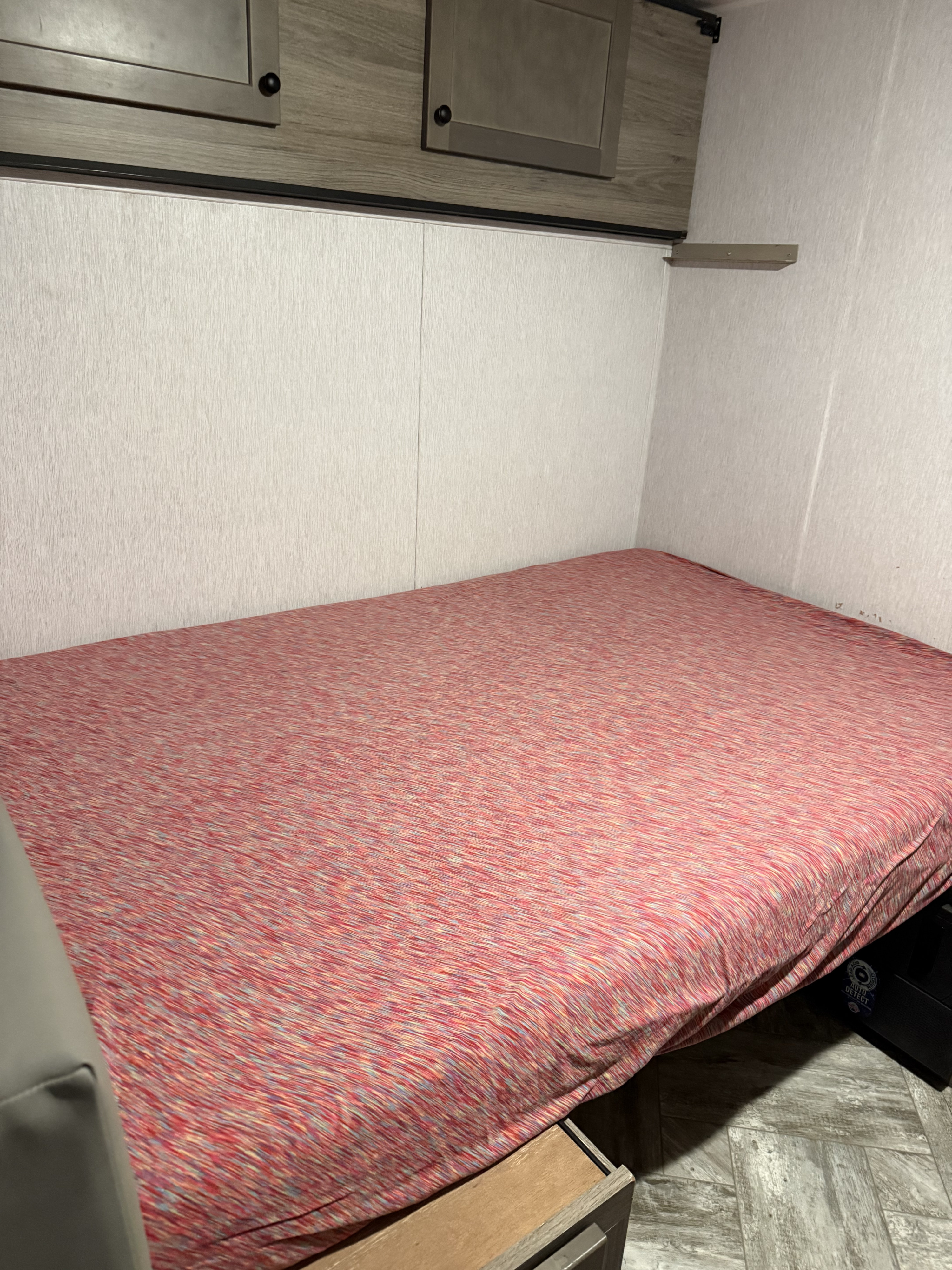 RV rental bedroom with a neatly made bed and overhead storage cabinets, offering a compact and cozy sleeping area for travel.. Sunset RV park Sunray 129 2025