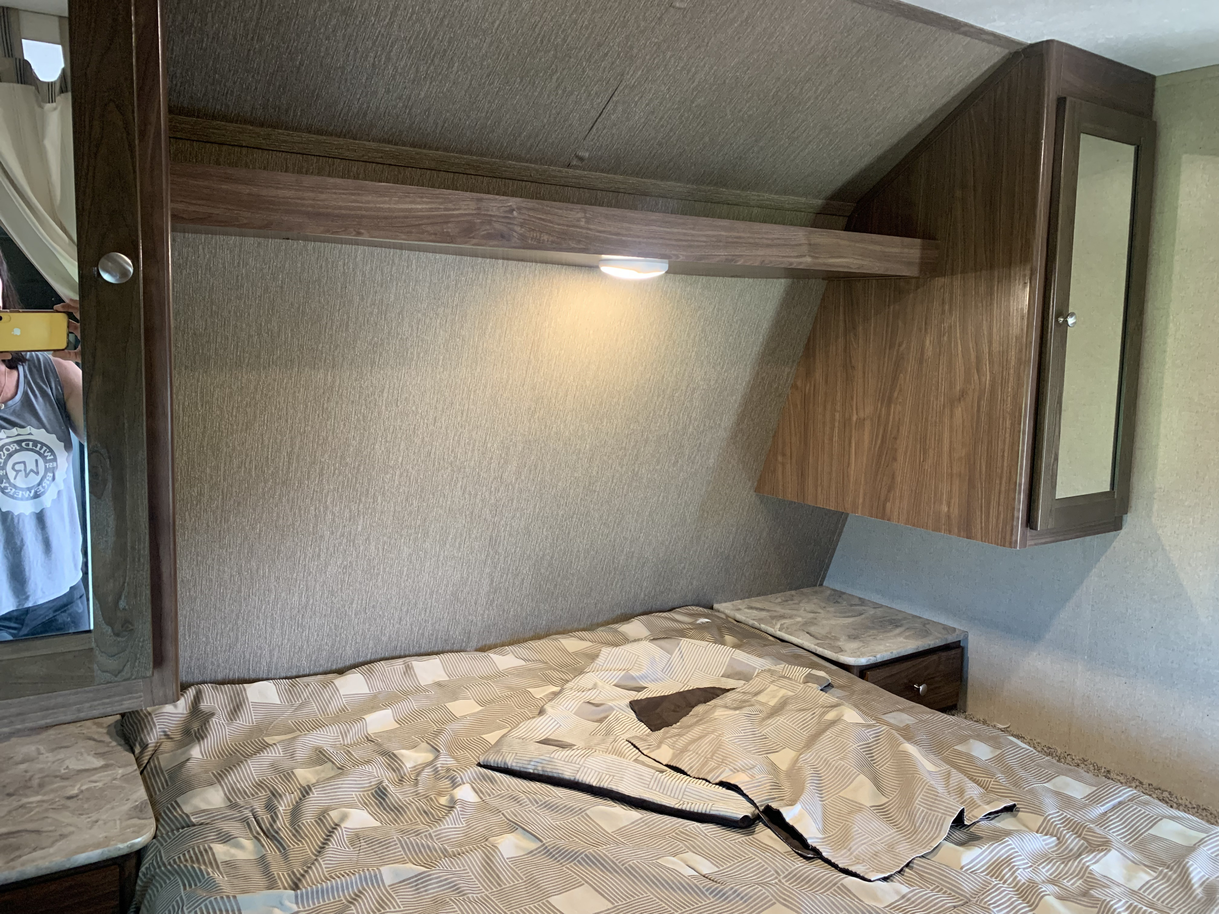 Compact RV rental bedroom featuring a patterned bed, overhead shelf with light, and mirrored storage. Ideal for travelers.. Dutchmen Coleman Lantern 2017