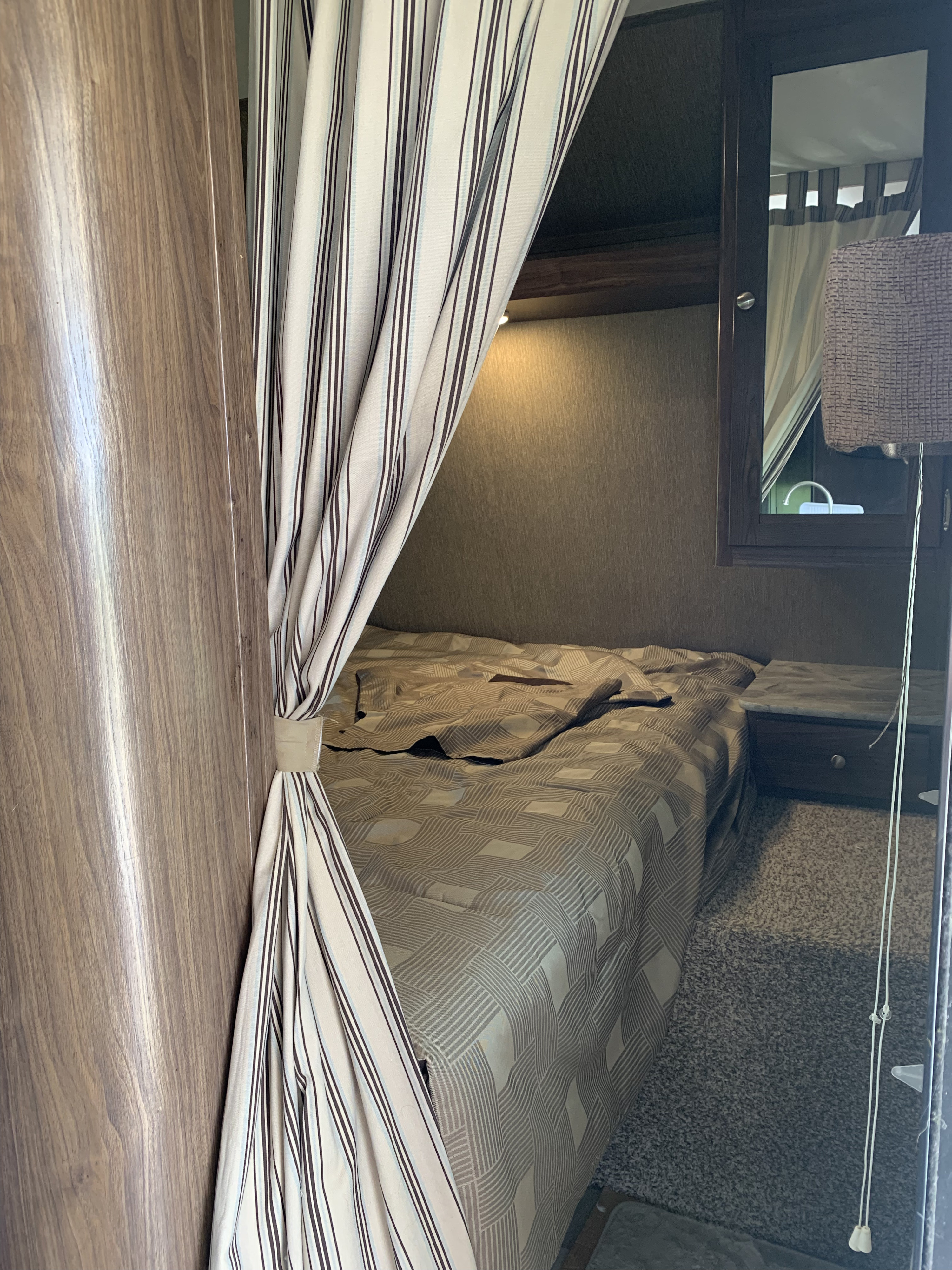 Cozy RV rental bedroom interior with a patterned bed, striped privacy curtains tied back, and a nightstand.. Dutchmen Coleman Lantern 2017