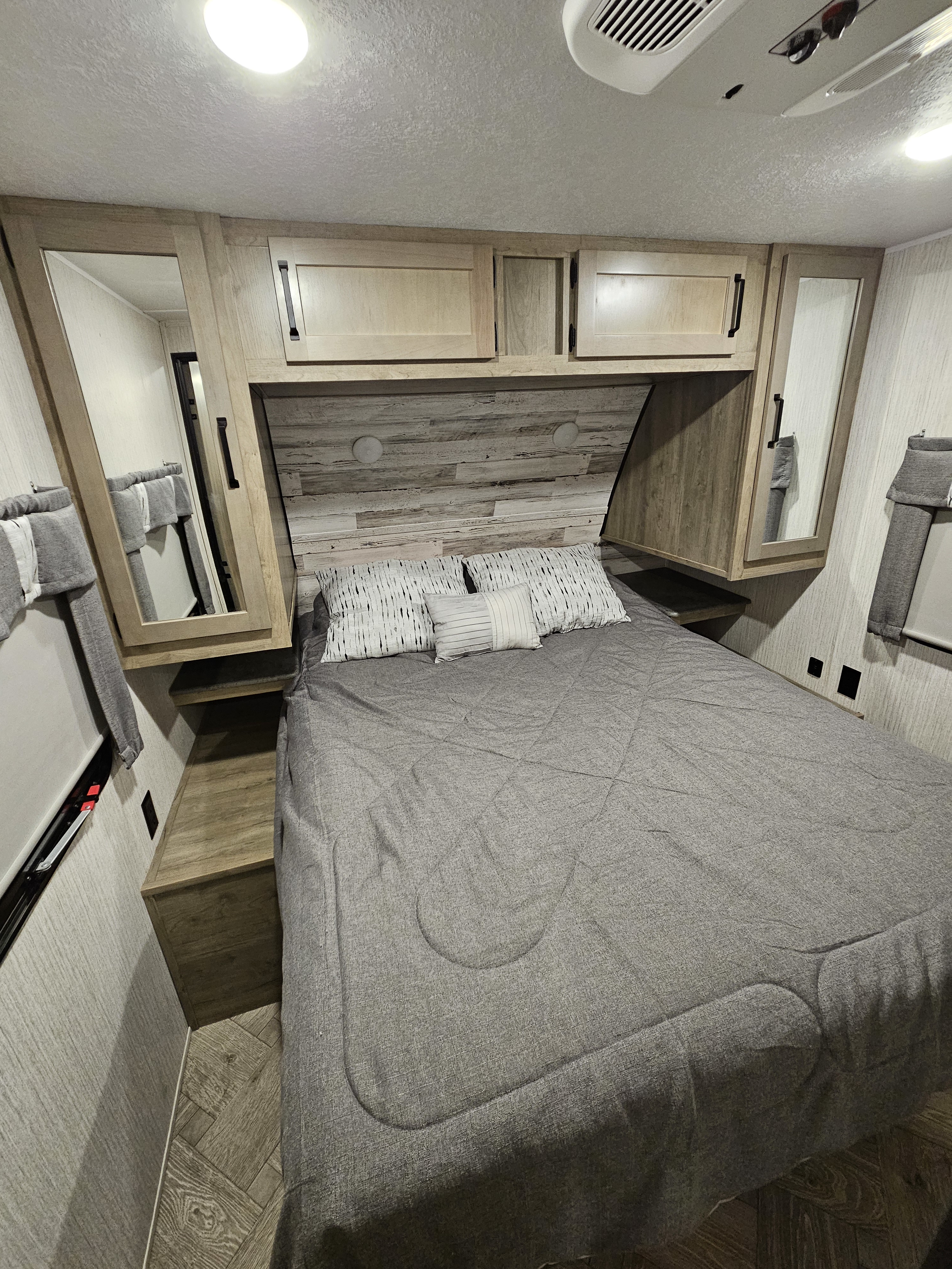 This inviting RV rental bedroom features a comfy grey bed, wooden headboard, and overhead storage for travel comfort.. Forest River Palomino Puma 2022