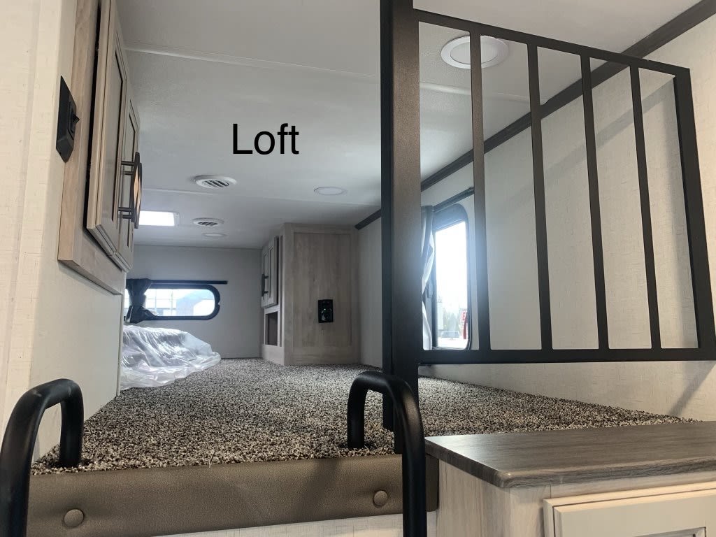 RV rental loft: A carpeted bunk bed sleeping area inside an RV, featuring a safety railing and window.. Forest River Sandpiper 2024