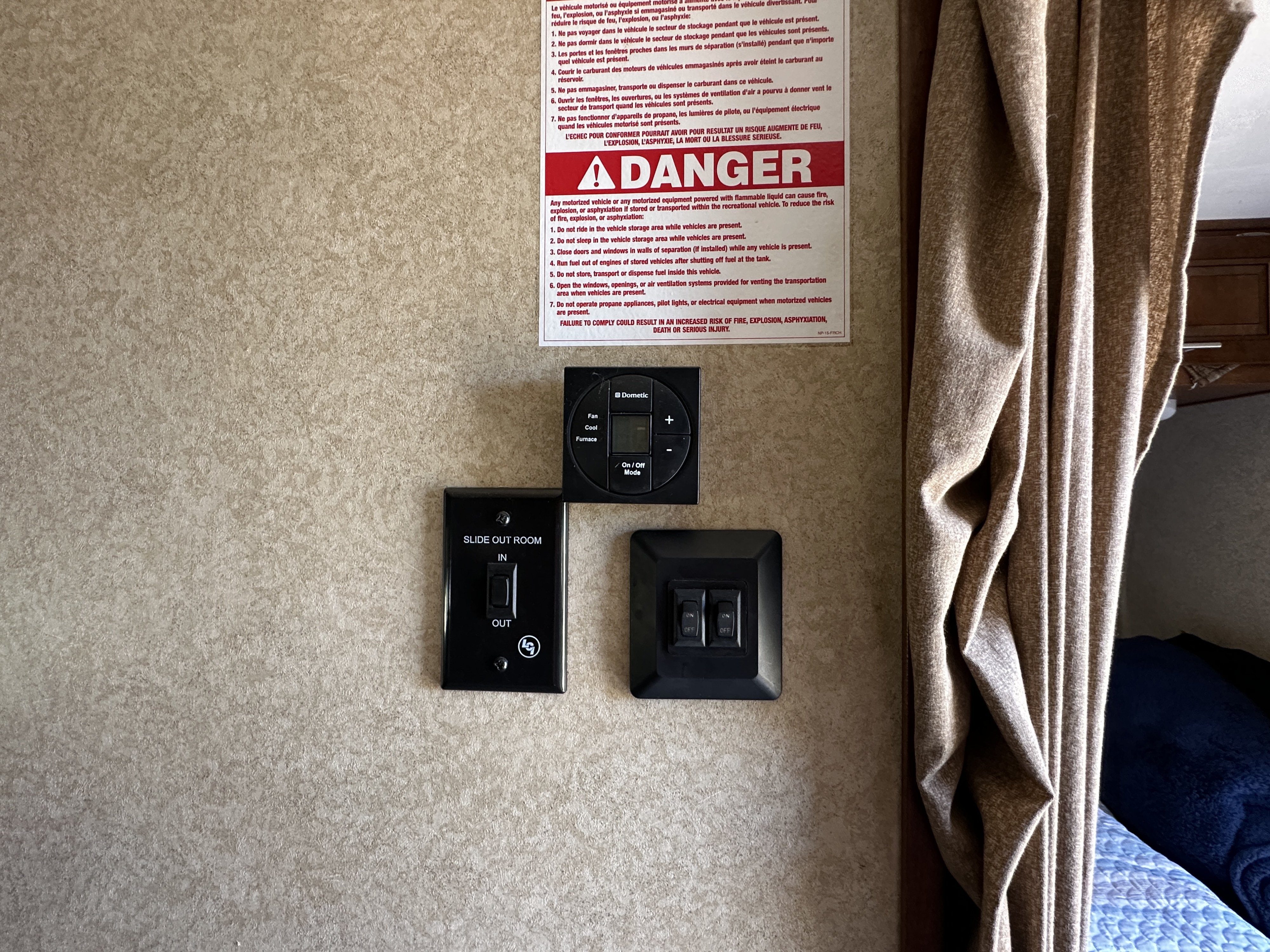 An RV rental interior wall displays a safety DANGER sign, Dometic thermostat, and slide-out controls next to a curtain.. Forest River Xlr Thunrderbolt 2013