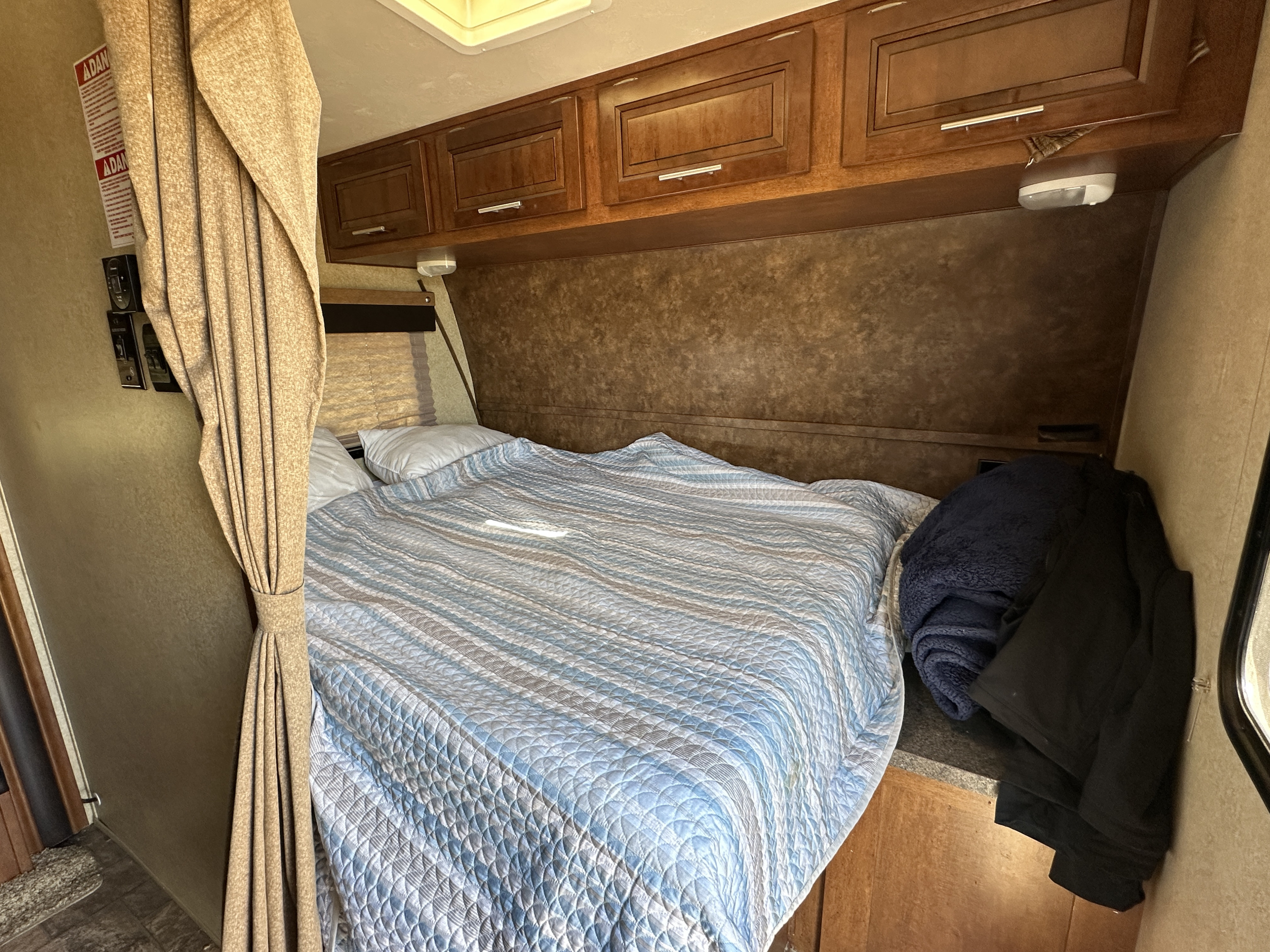 Inside an RV rental: a comfortable sleeping area with a blue quilted bed, wood cabinets, and tied-back curtains.. Forest River Xlr Thunrderbolt 2013
