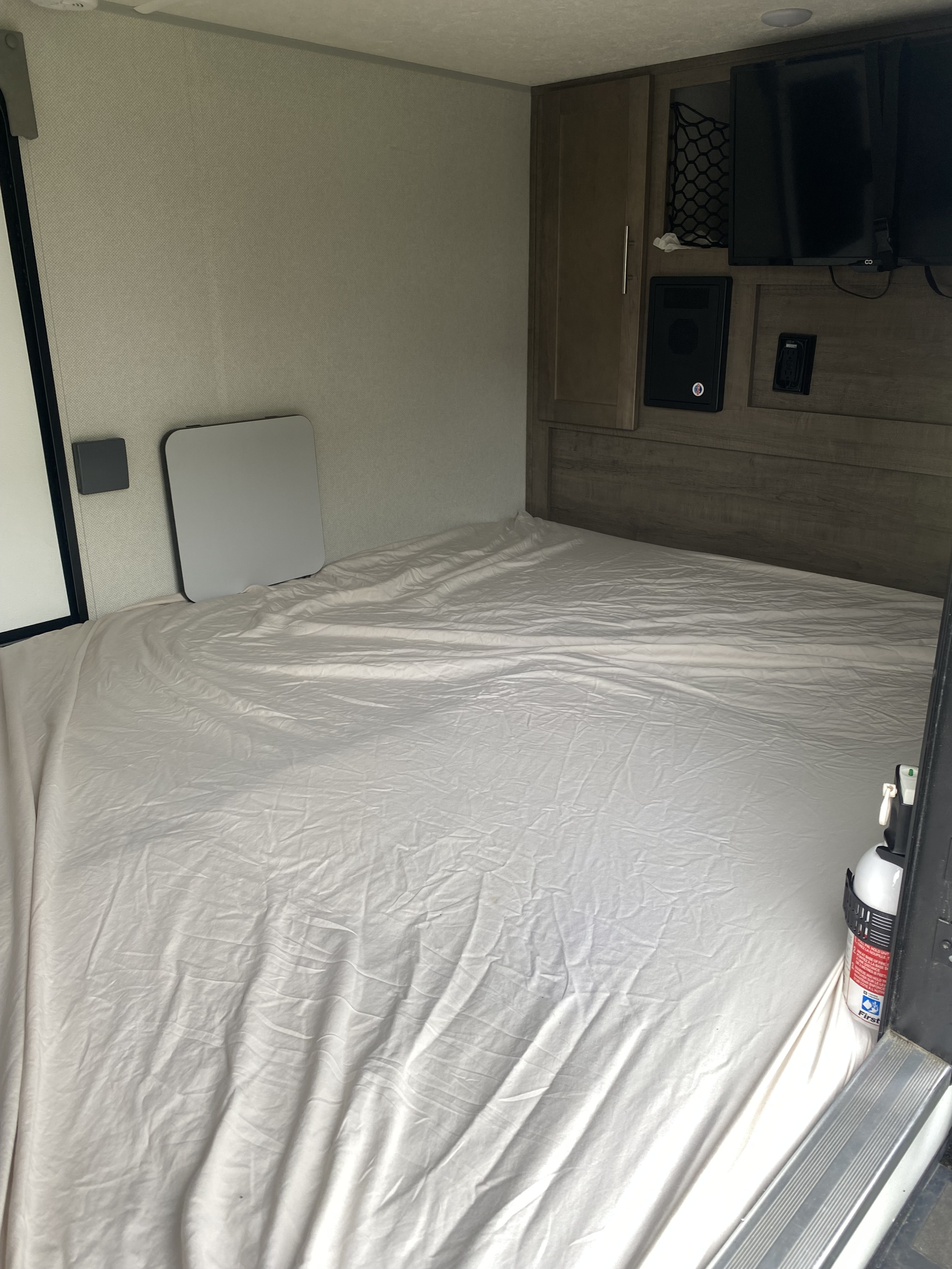 RV rental bedroom: a comfortable bed with white sheets, headboard with TV, built-in storage, and a small side table on left.. Forest River Other 2019