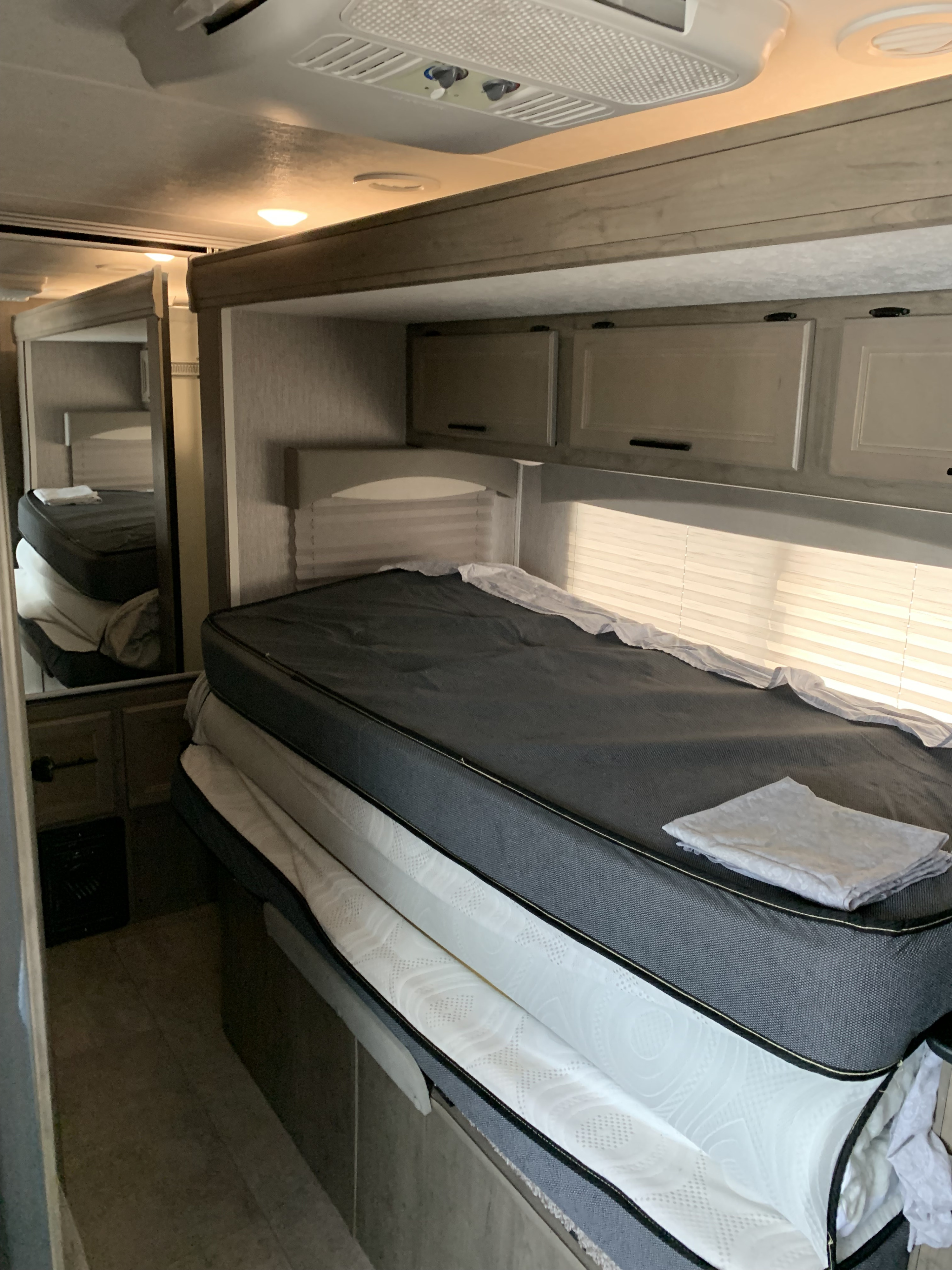 RV rental bunk room with stacked mattresses and overhead cabinets. A mirror reflects another bunk, indicating multiple sleeping spots.. Coachmen Freelander 2021