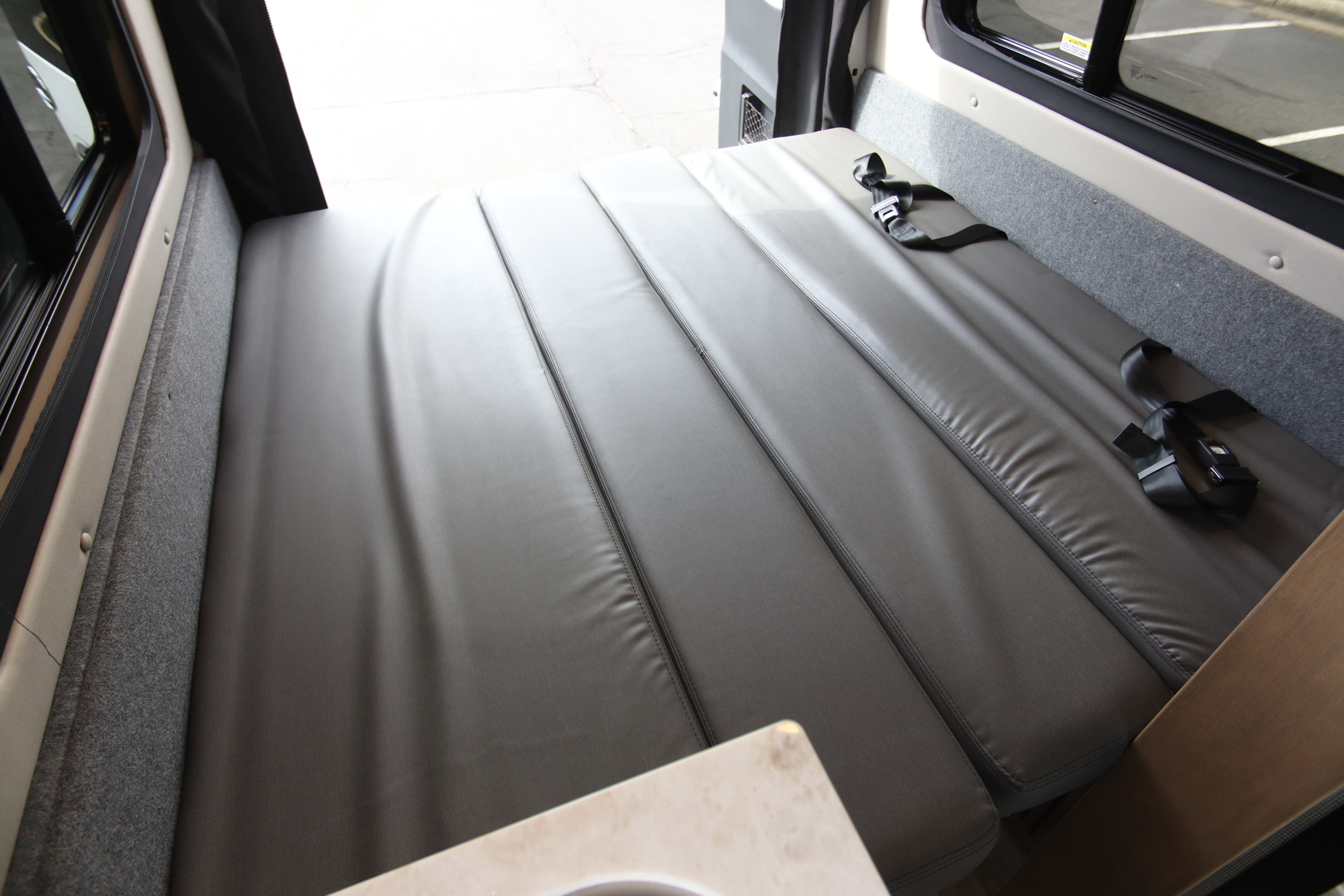 Interior of an RV rental showing a spacious, flexible gray bed/seating area with seatbelts. Ideal for travel and comfy nights.. Tiffin Motorhomes Cahaba 2022
