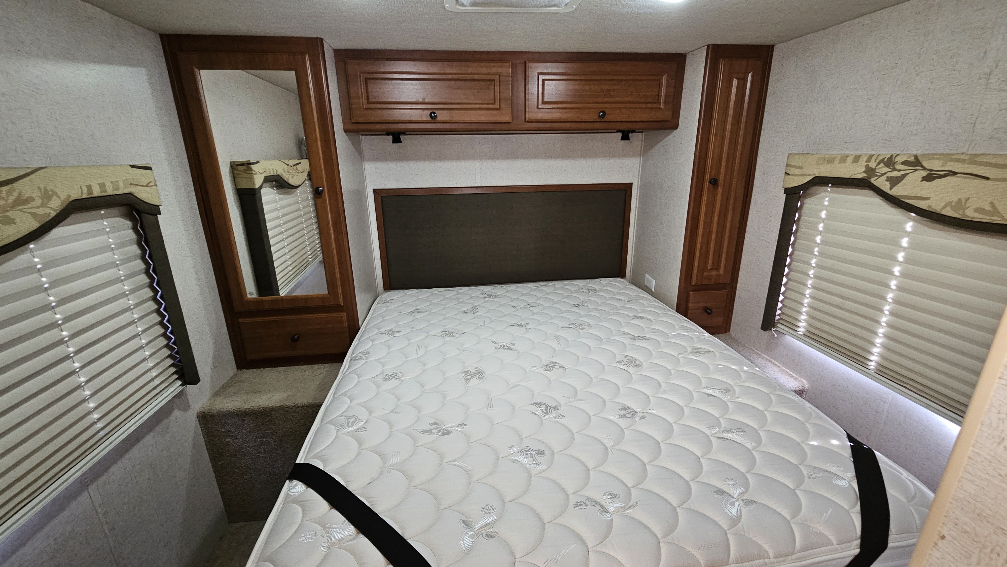 Cozy RV rental bedroom with a white mattress, rich wood cabinets, and window blinds, offering a compact sleeping space.. Tioga Ranger 2009