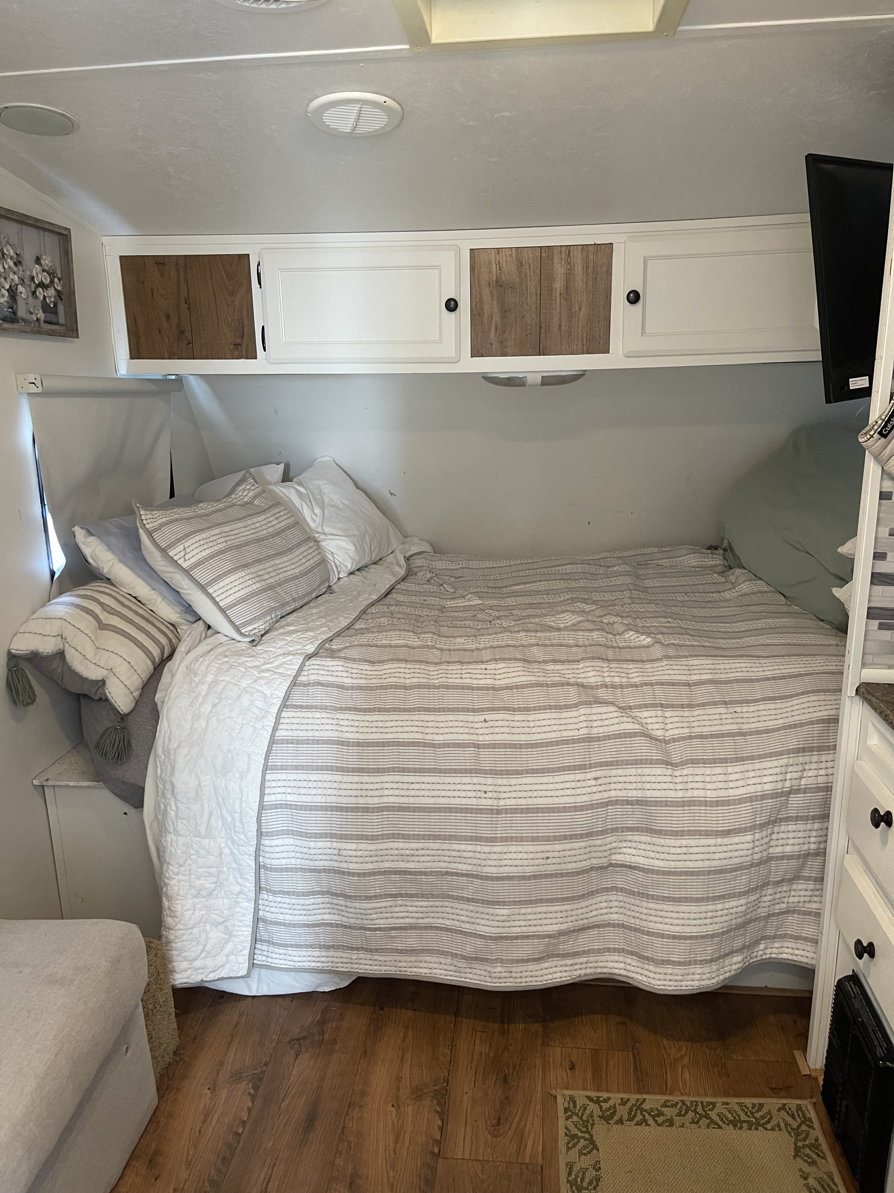 Cozy RV rental bedroom interior featuring a bed with striped quilt, white overhead cabinets, and wood flooring.. Nomad Nomad Trailer 2010