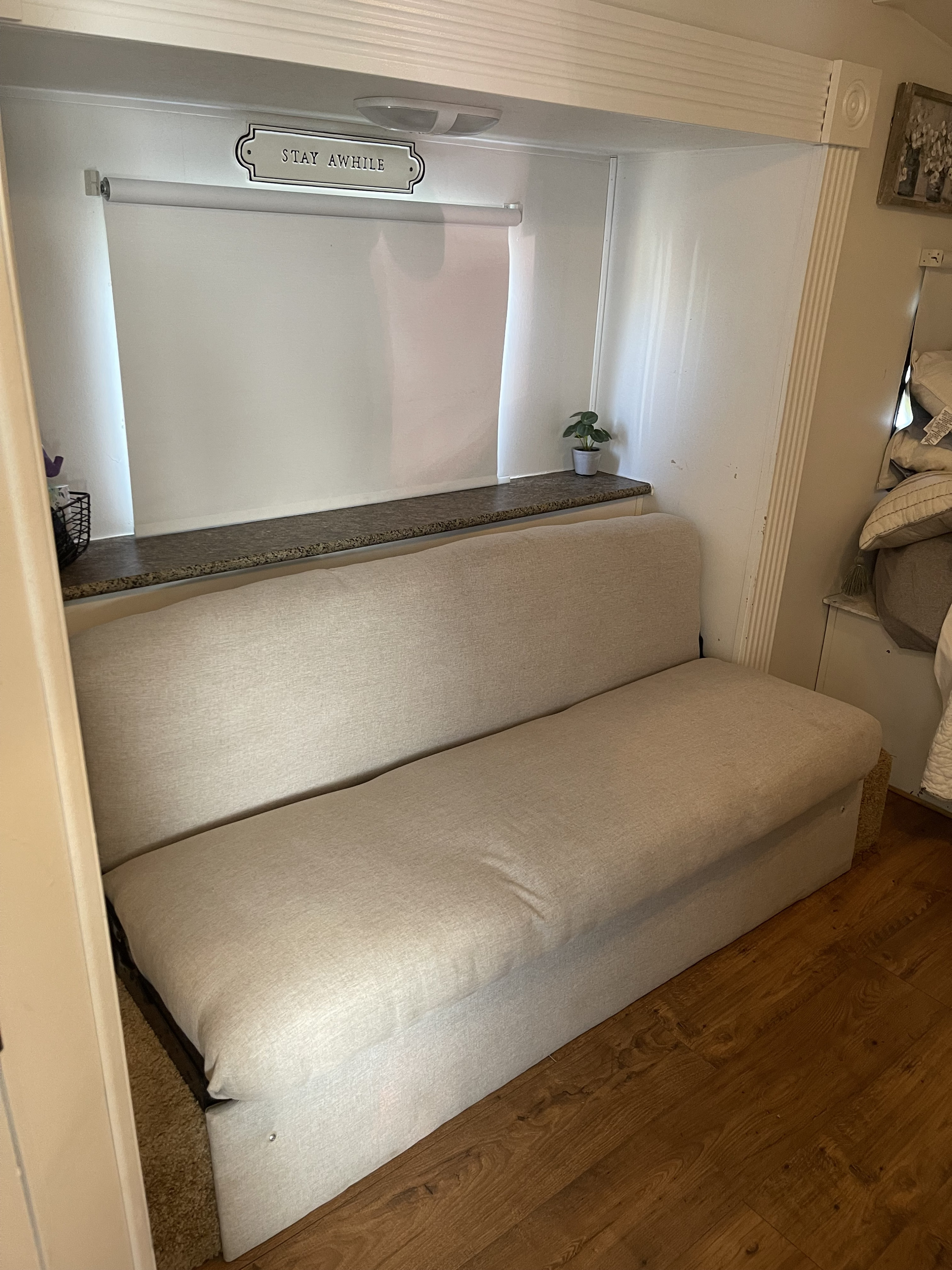 RV rental living space: a light beige sofa, built-in shelf, and window with a "STAY AWHILE" sign.. Nomad Nomad Trailer 2010