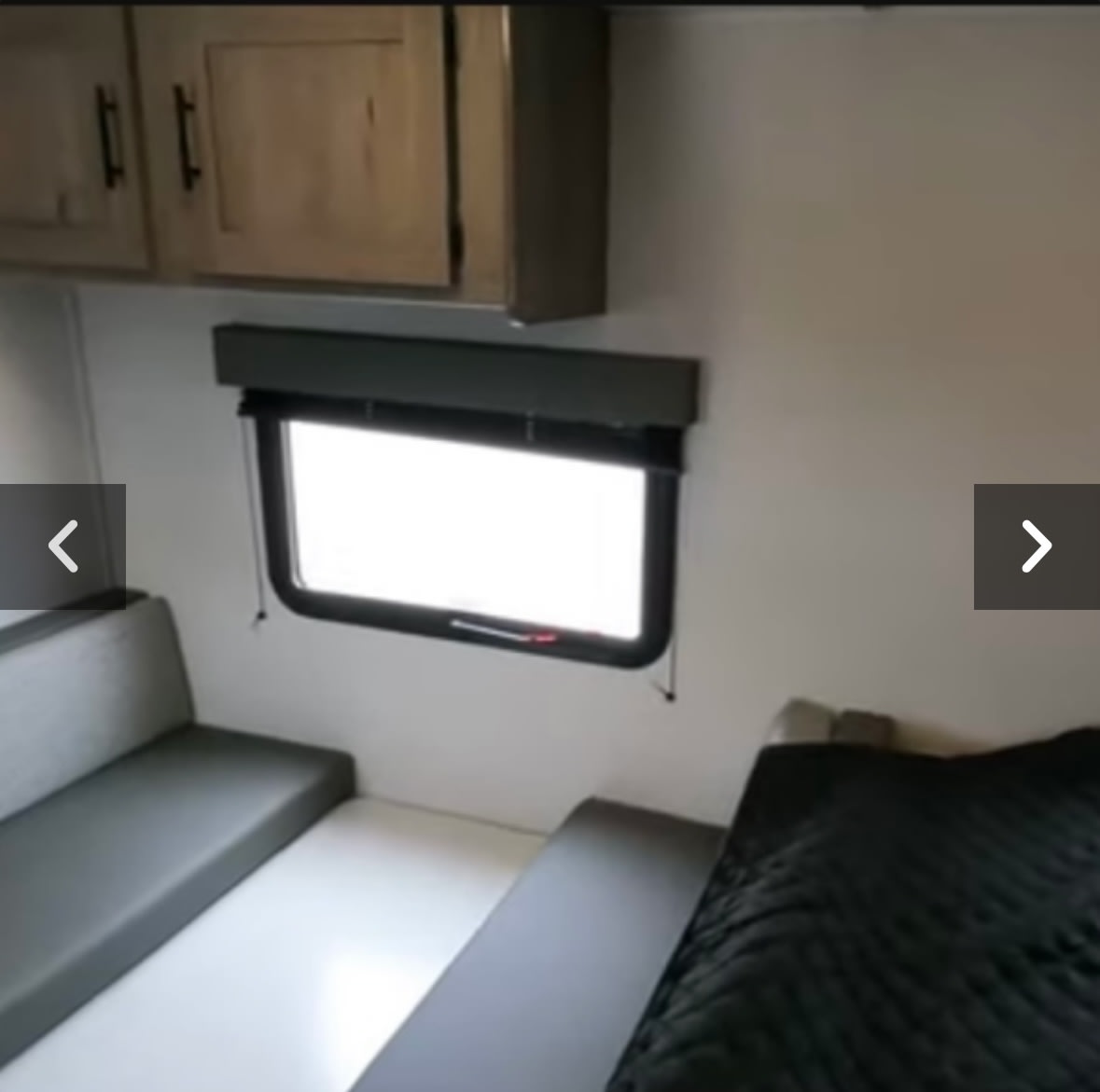 RV rental interior: cozy bed, bench seating, and cabinets visible. A bright window offers light in this compact space.. Keystone RV Springdale 2021