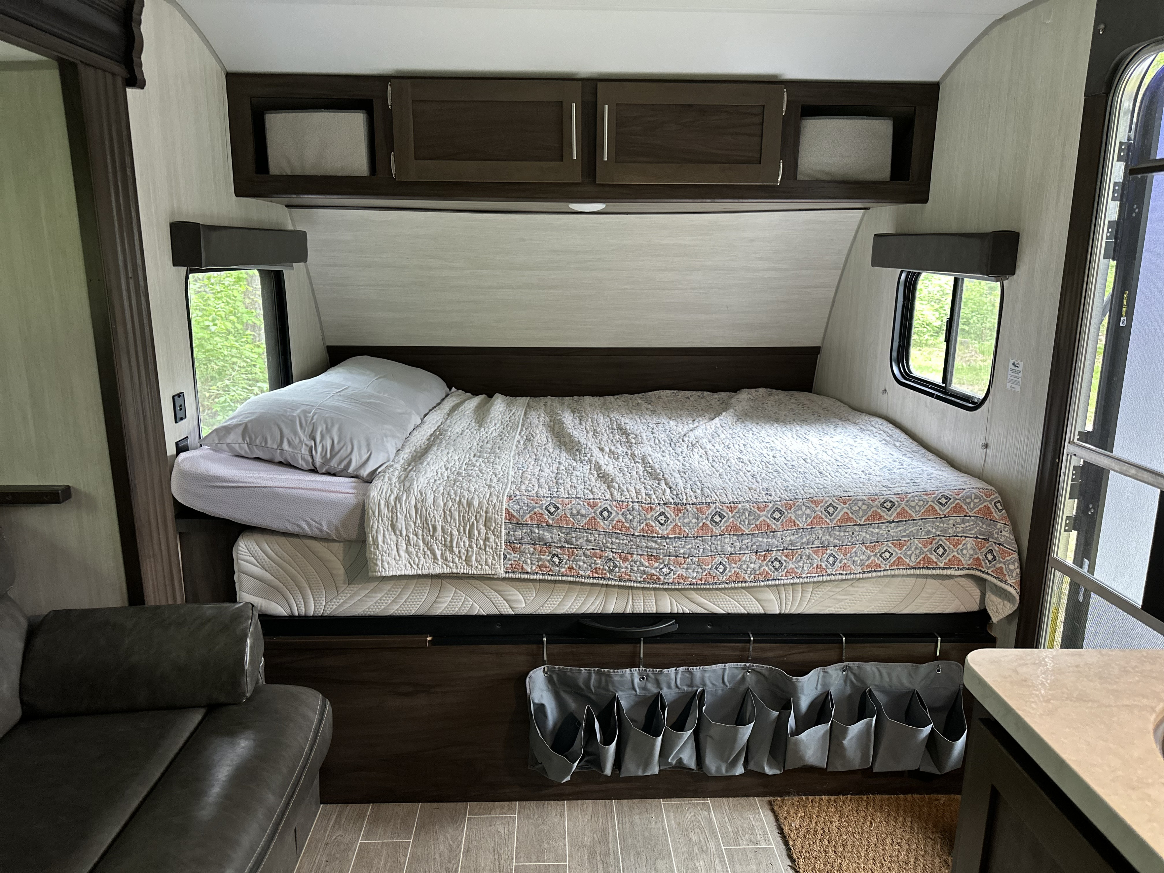 Cozy rv rental interior featuring a comfortable bed with quilt, overhead cabinets, and a convenient hanging storage organizer.. Forest River Cherokee Wolf Pup 2020
