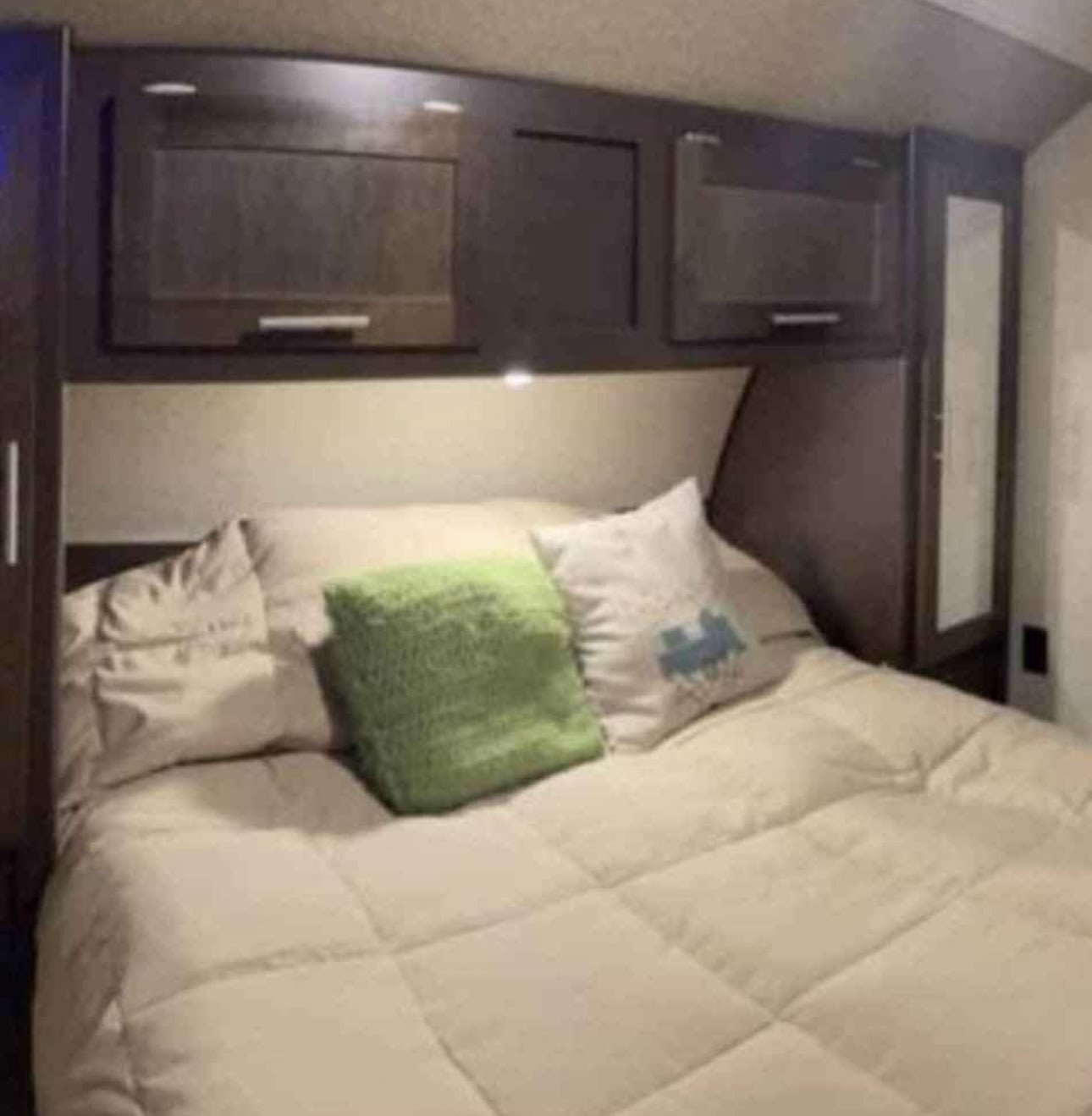 RV rental bedroom showcasing a cozy bed with beige bedding, green & patterned pillows, and dark wood overhead cabinets.. Forest River Cherokee Grey Wolf 2016