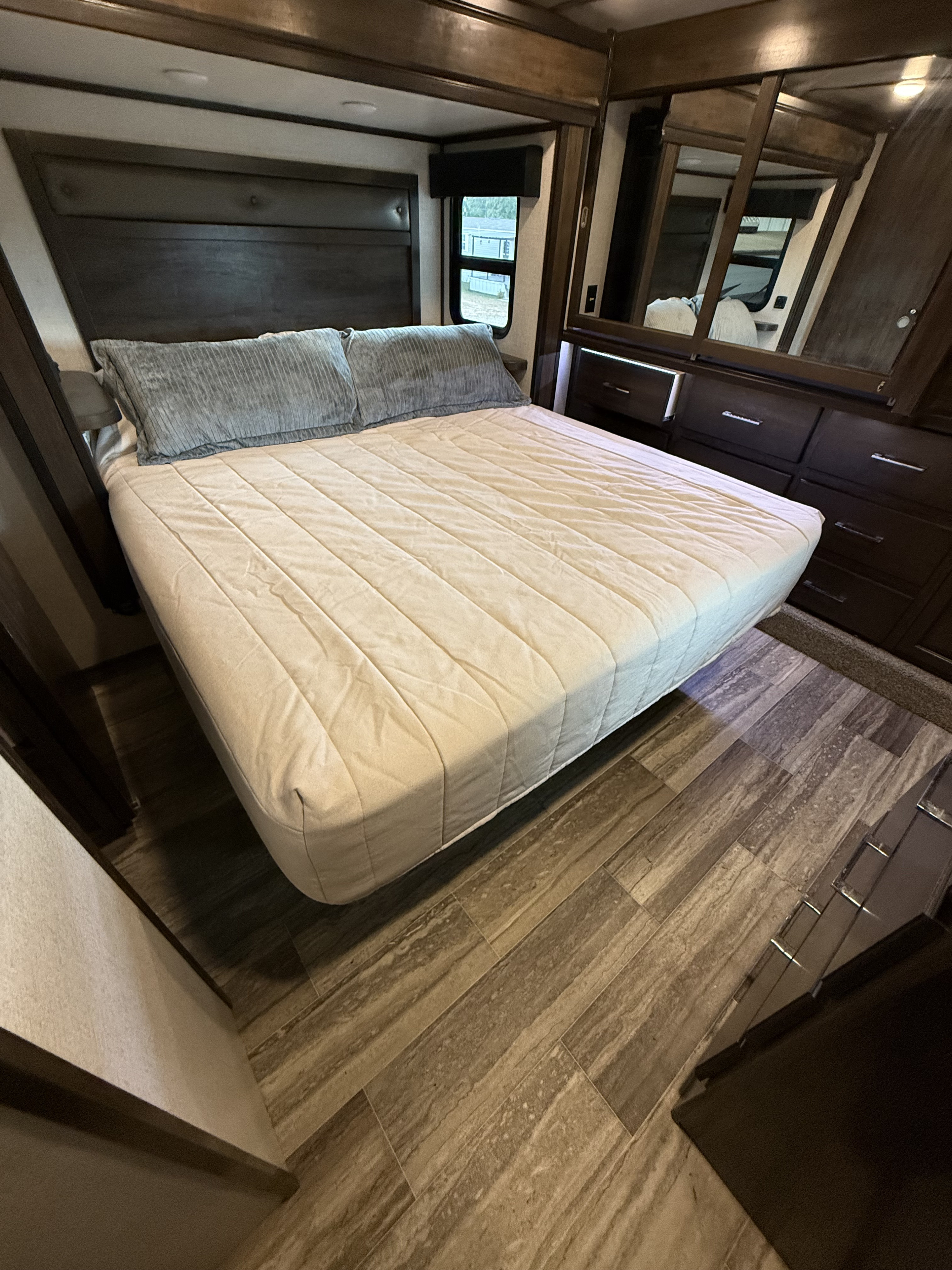 Spacious RV rental bedroom with a comfy bed, dark wood headboard, dresser, and wood-look flooring.. Dutchmen Yukon 2022