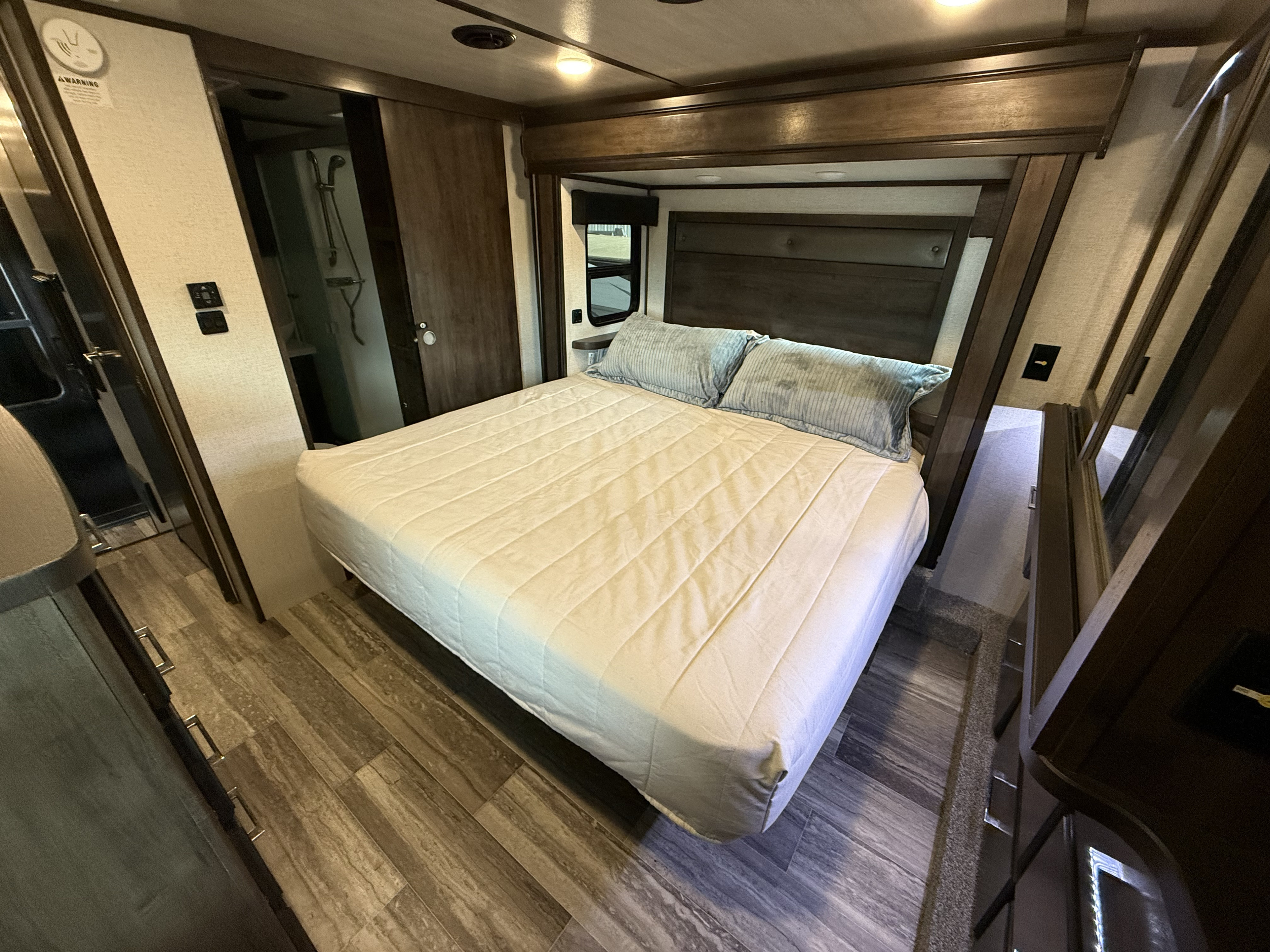 Spacious RV rental bedroom featuring a queen bed, wood-look flooring, and a connecting bathroom, ideal for comfortable travel.. Dutchmen Yukon 2022
