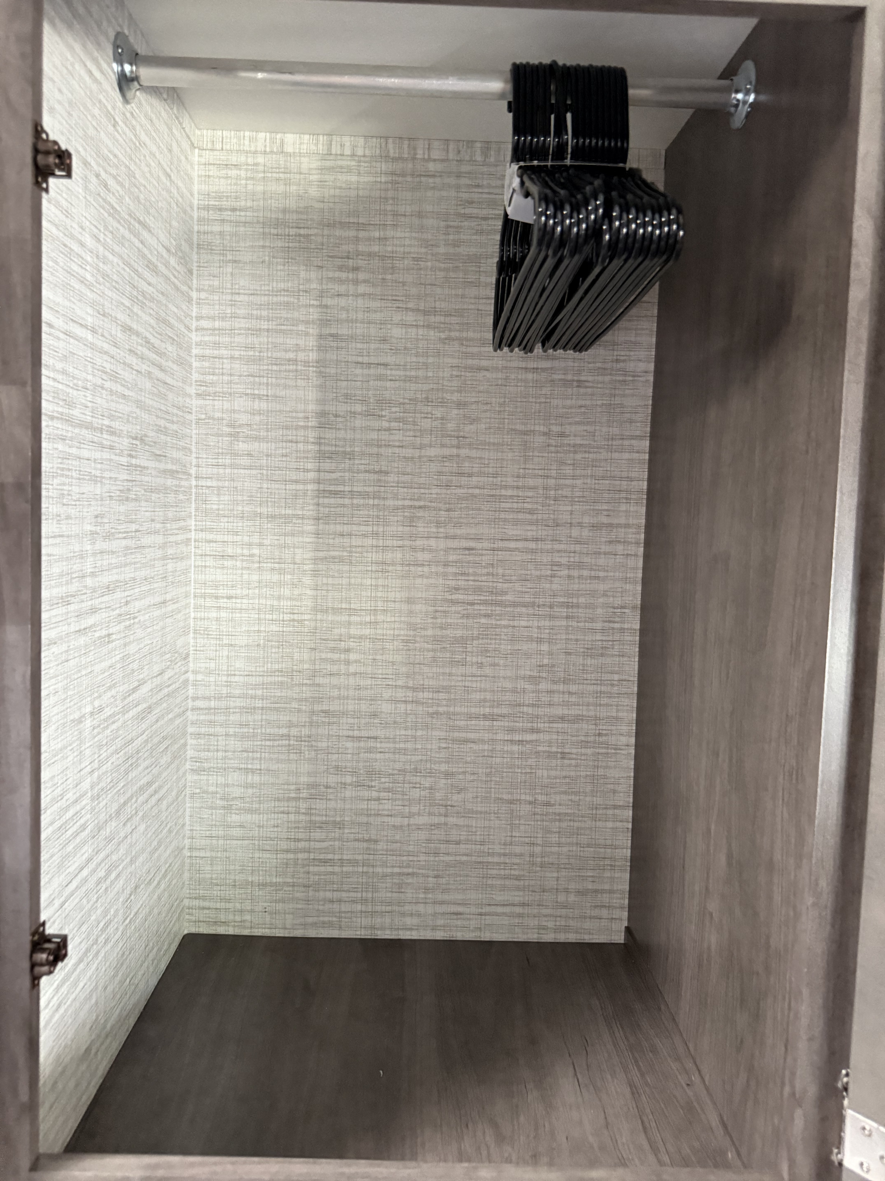 The inside of an empty, compact RV rental closet. It features a hanging rod with new black hangers and textured walls.. Entegra Odyssey 2025