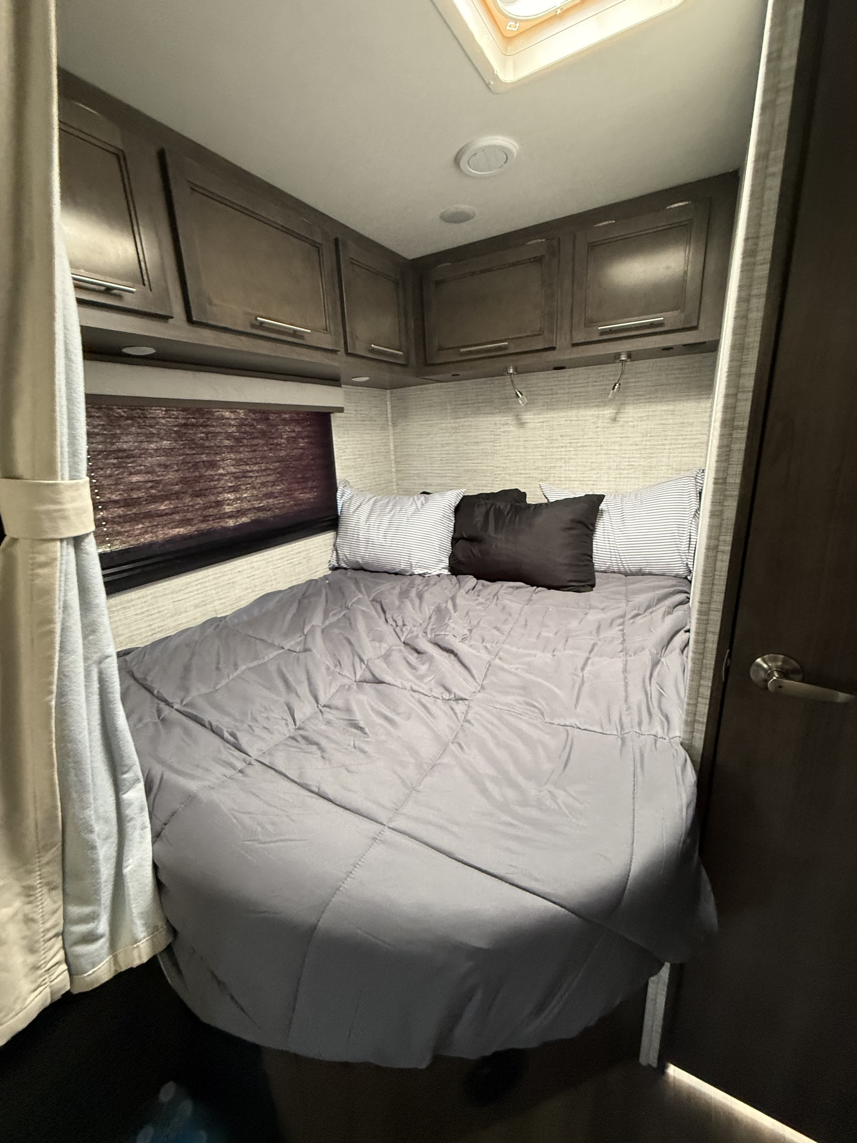 Explore this compact RV rental bedroom featuring a comfy bed with gray bedding, overhead storage, and a window for scenic views.. Entegra Odyssey 2025