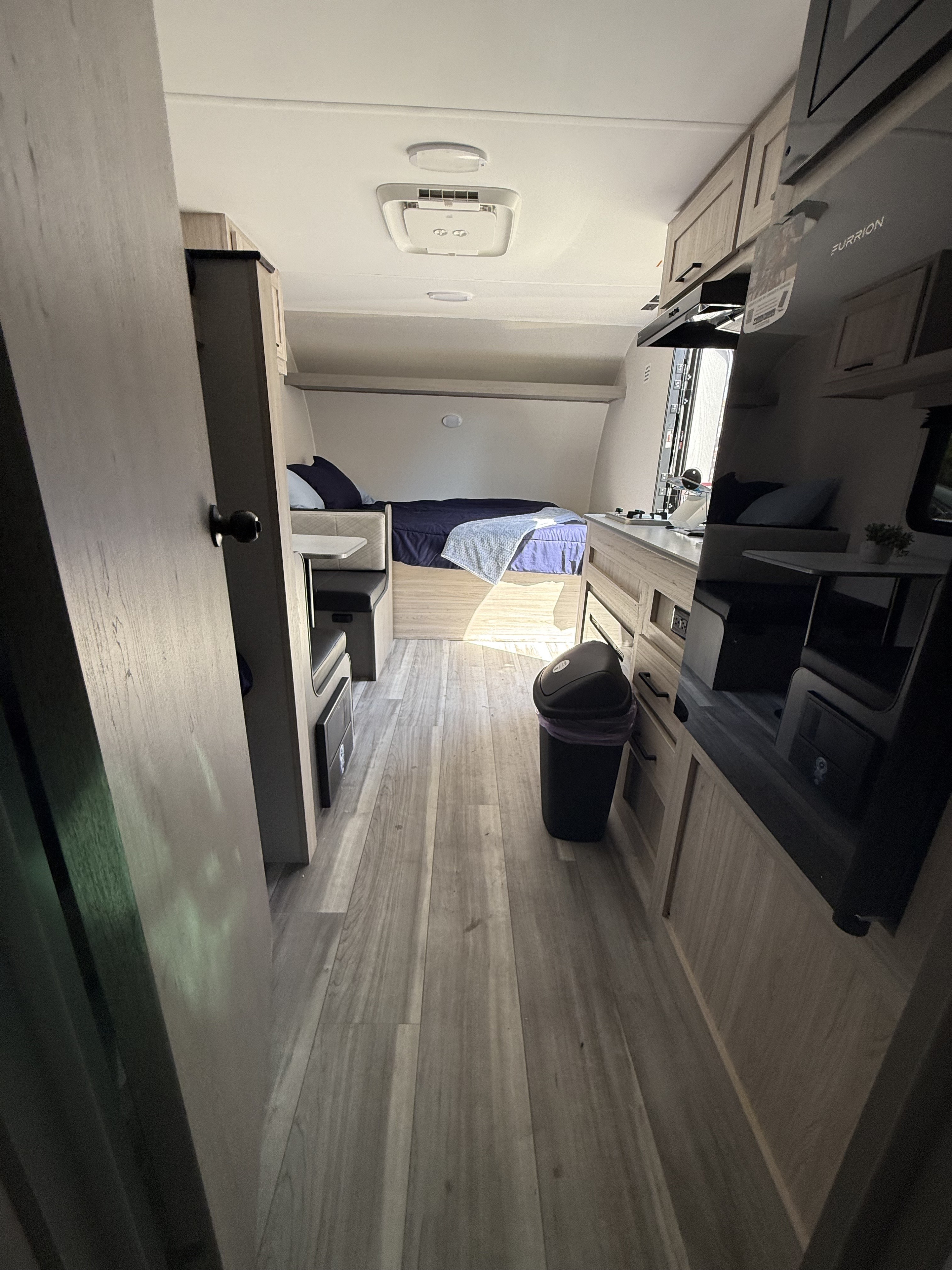 Bright rv rental interior, with wood-look floors, a bed, dinette, & kitchen area, seen from the entrance.. Heartland Pioneer 2025