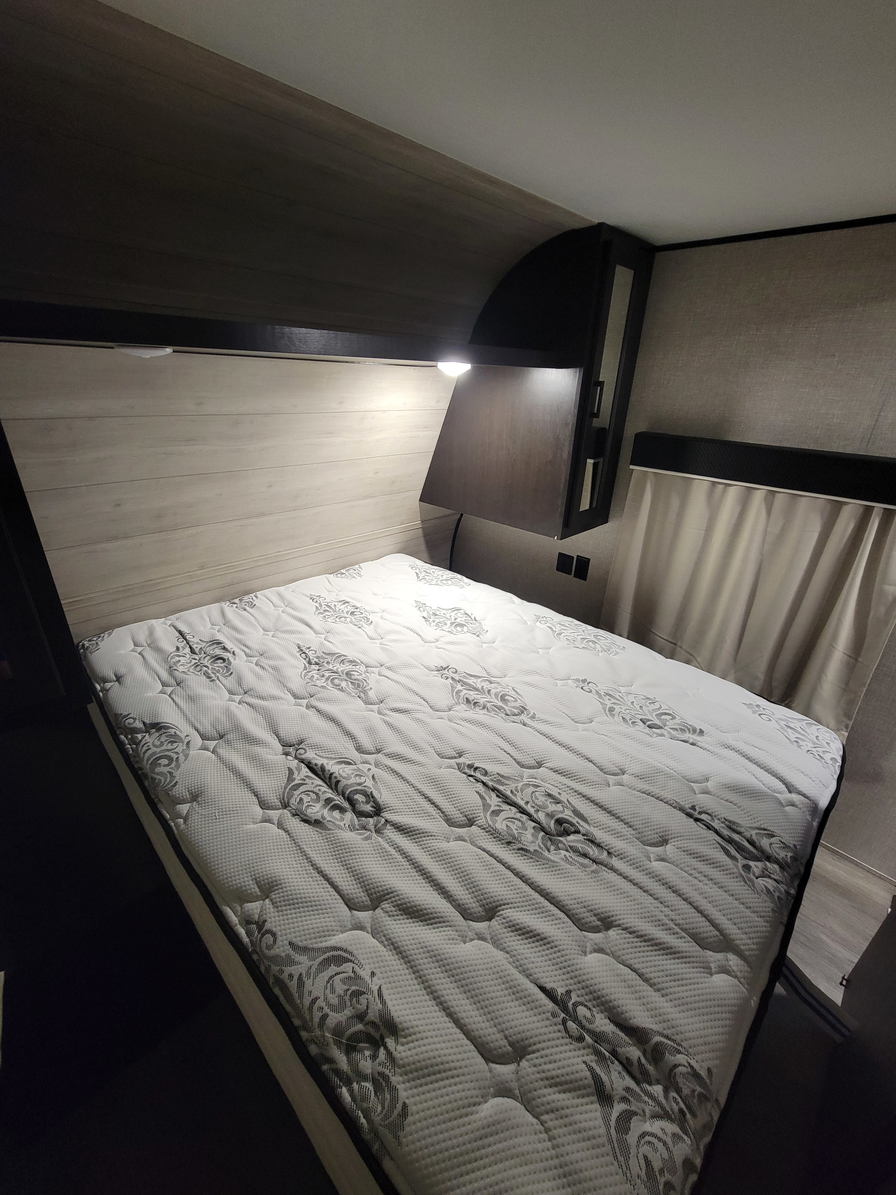 Compact RV rental bedroom featuring a patterned mattress, wood headboard, and reading light for a cozy stay.. Jayco Jay Flight SLX 2022
