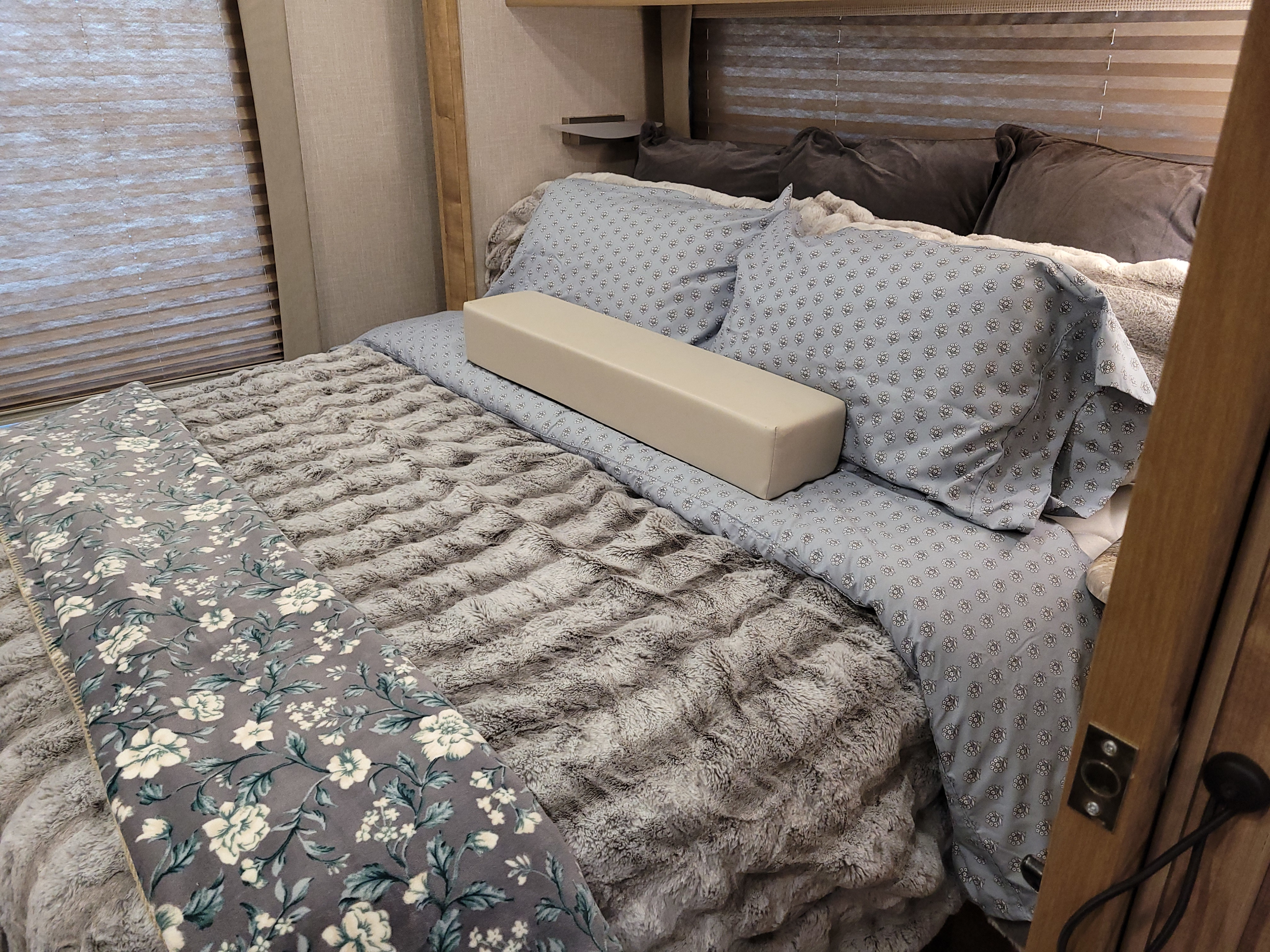 Cozy RV rental bedroom featuring soft patterned bedding, plush throws, and window blinds for a comfortable travel experience.. Coachmen Concord 2019