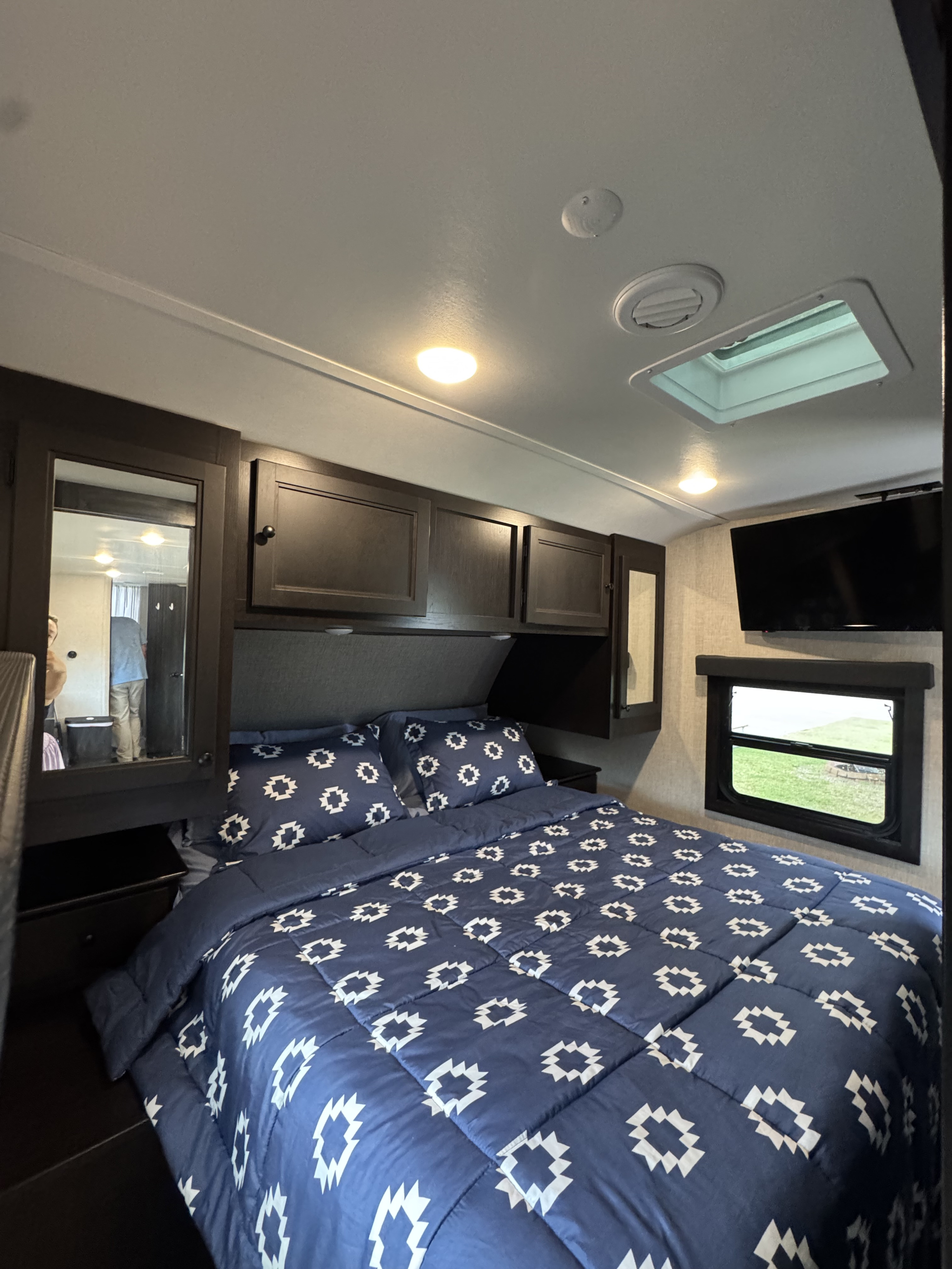 Inside a comfortable RV rental bedroom, featuring a navy patterned bed, mounted TV, and overhead storage. Ready for adventure!. Highland Ridge RV Range Lite 2023