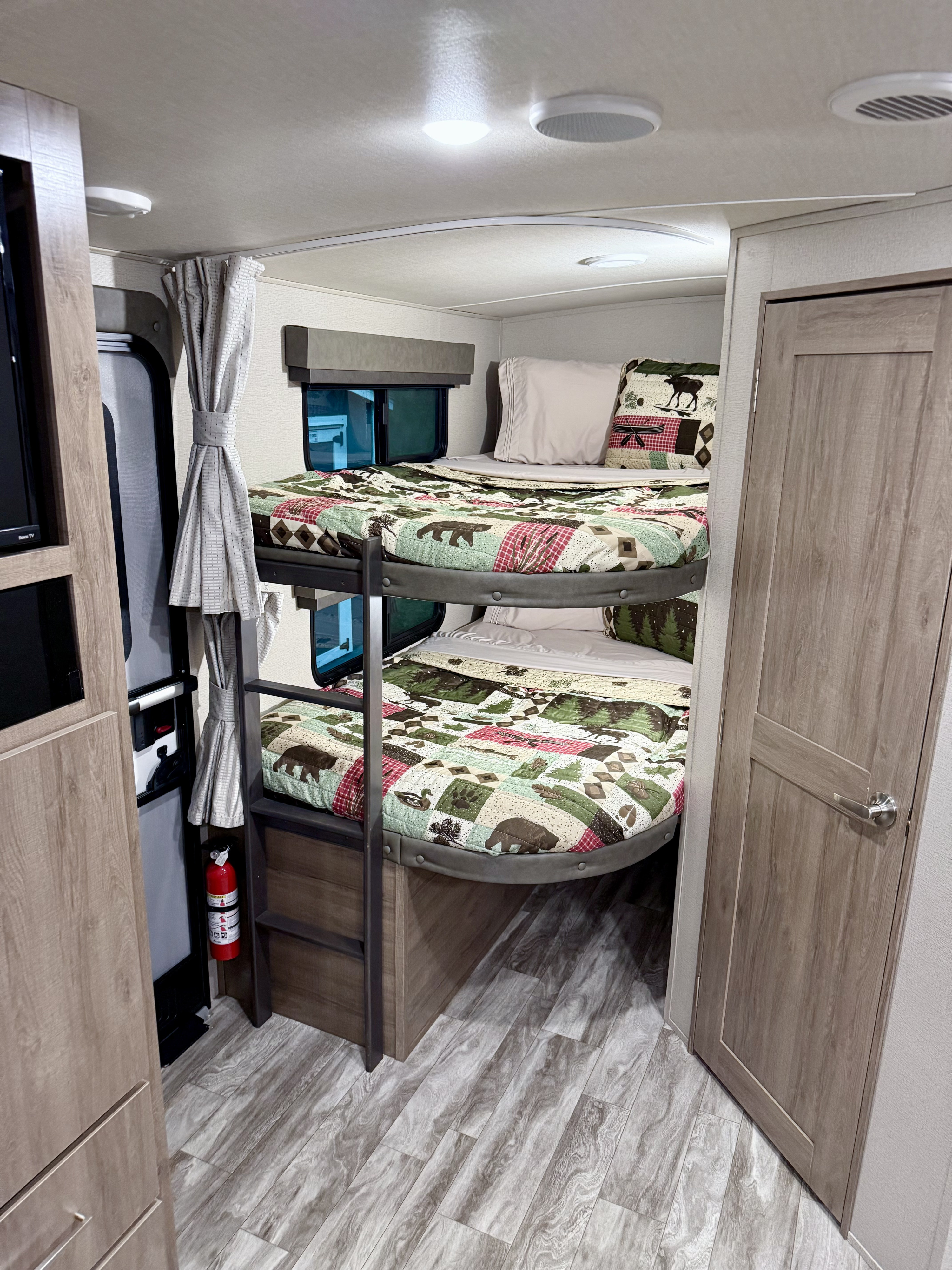 Cozy RV rental interior showing wilderness-themed bunk beds, windows, a fire extinguisher, and wood-look flooring.. Grand Design Imagine 2021