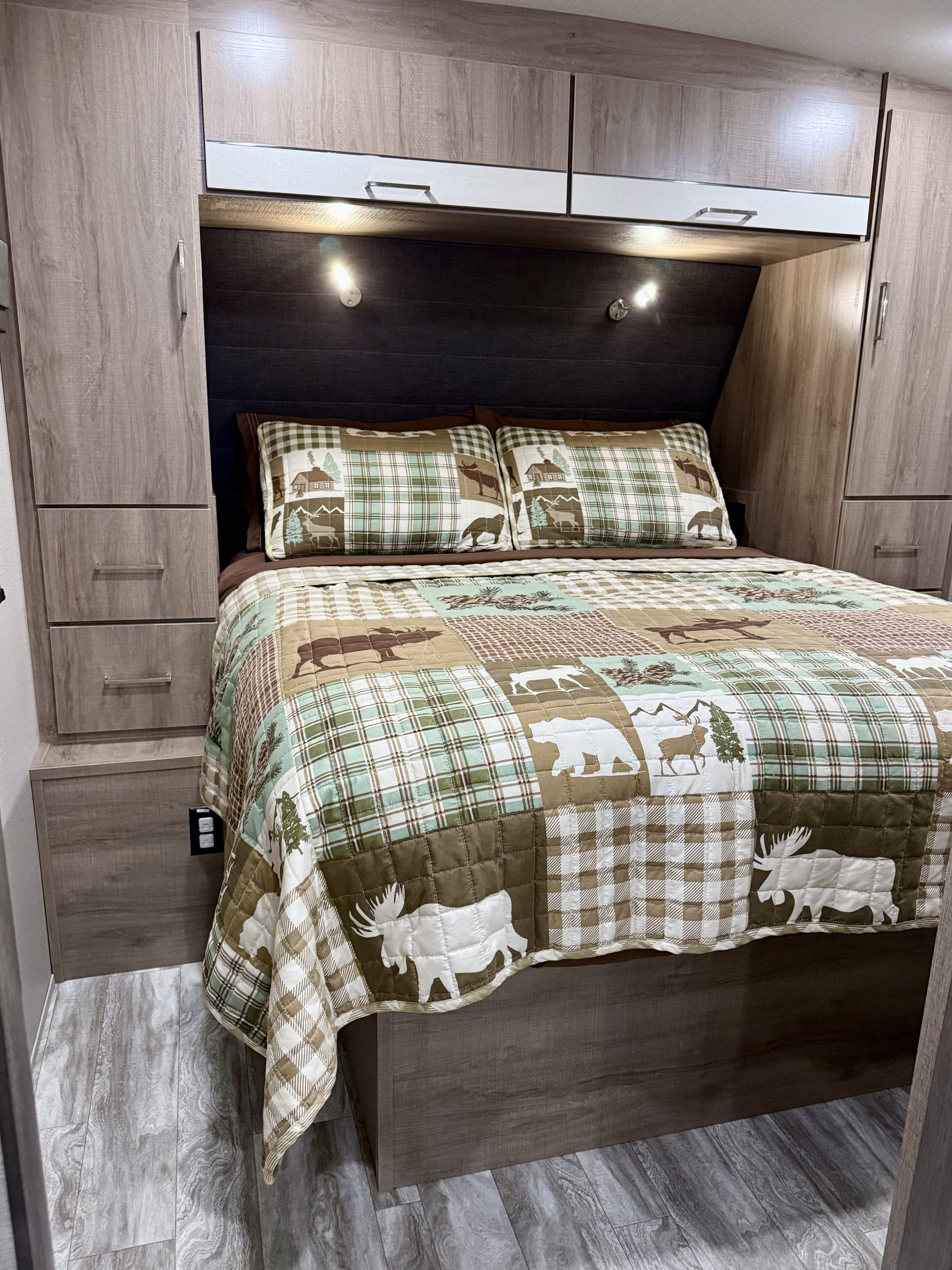 This RV rental features a cozy bedroom with plaid & animal-themed bedding, overhead cabinets, and side storage.. Grand Design Imagine 2021