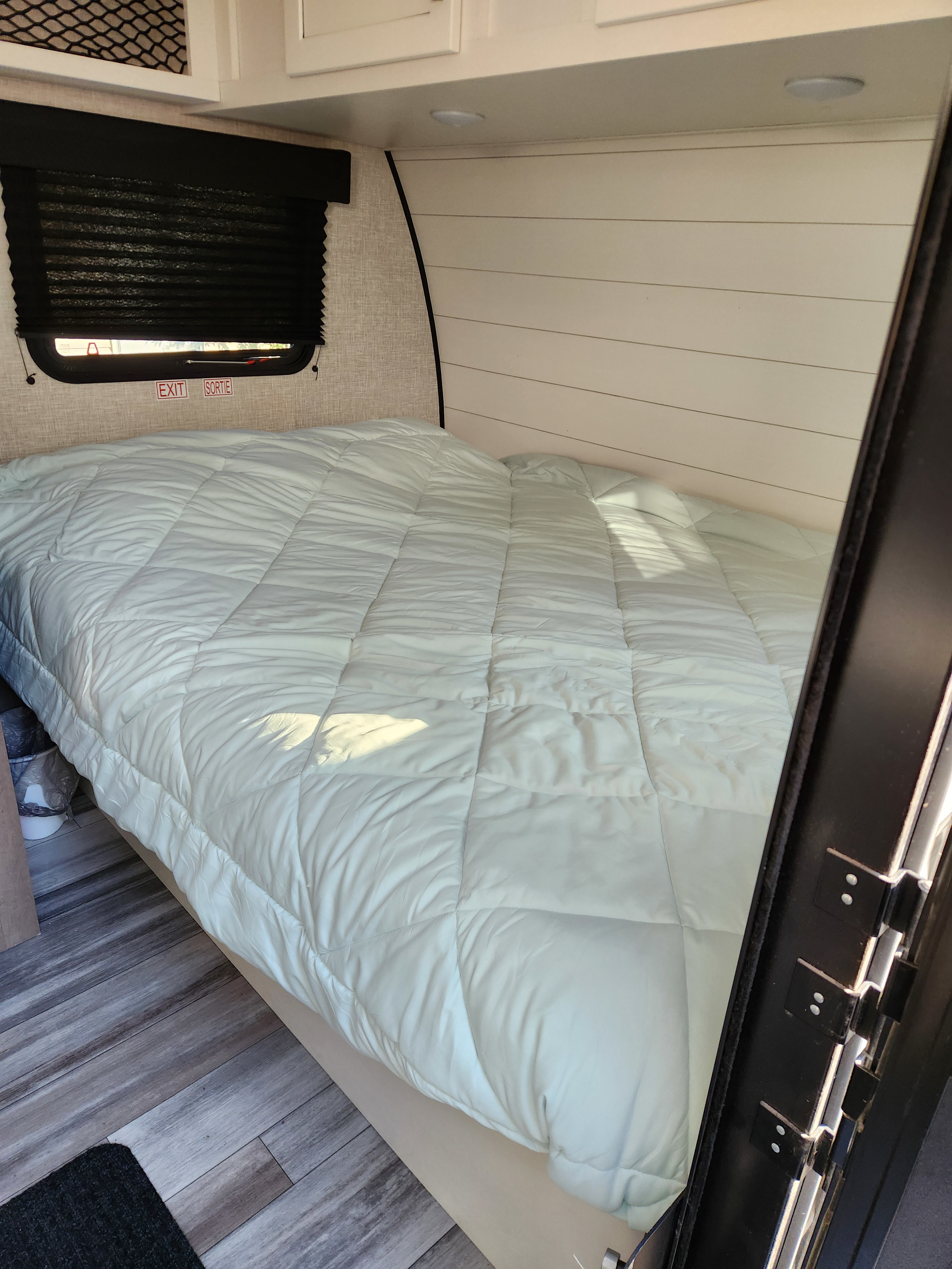 Interior view of an RV rental: a compact bedroom featuring a mint green bed, window with black shades, and wood-look floor.. Jayco Jay Flight Baja Edition 2024