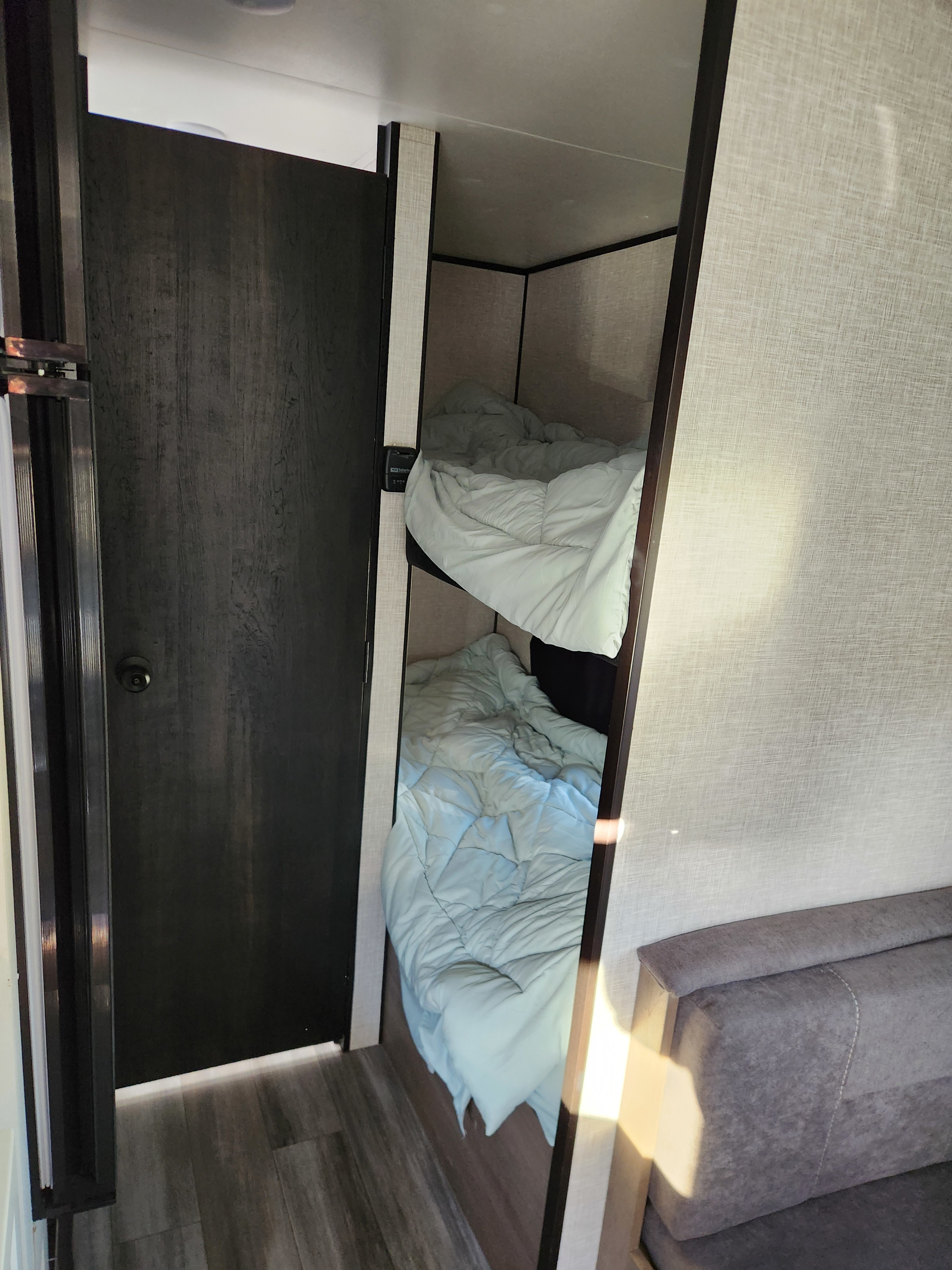 This RV rental features stacked bunk beds with light blue comforters, a dark door on the left, and textured walls, offering cozy sleeping.. Jayco Jay Flight Baja Edition 2024