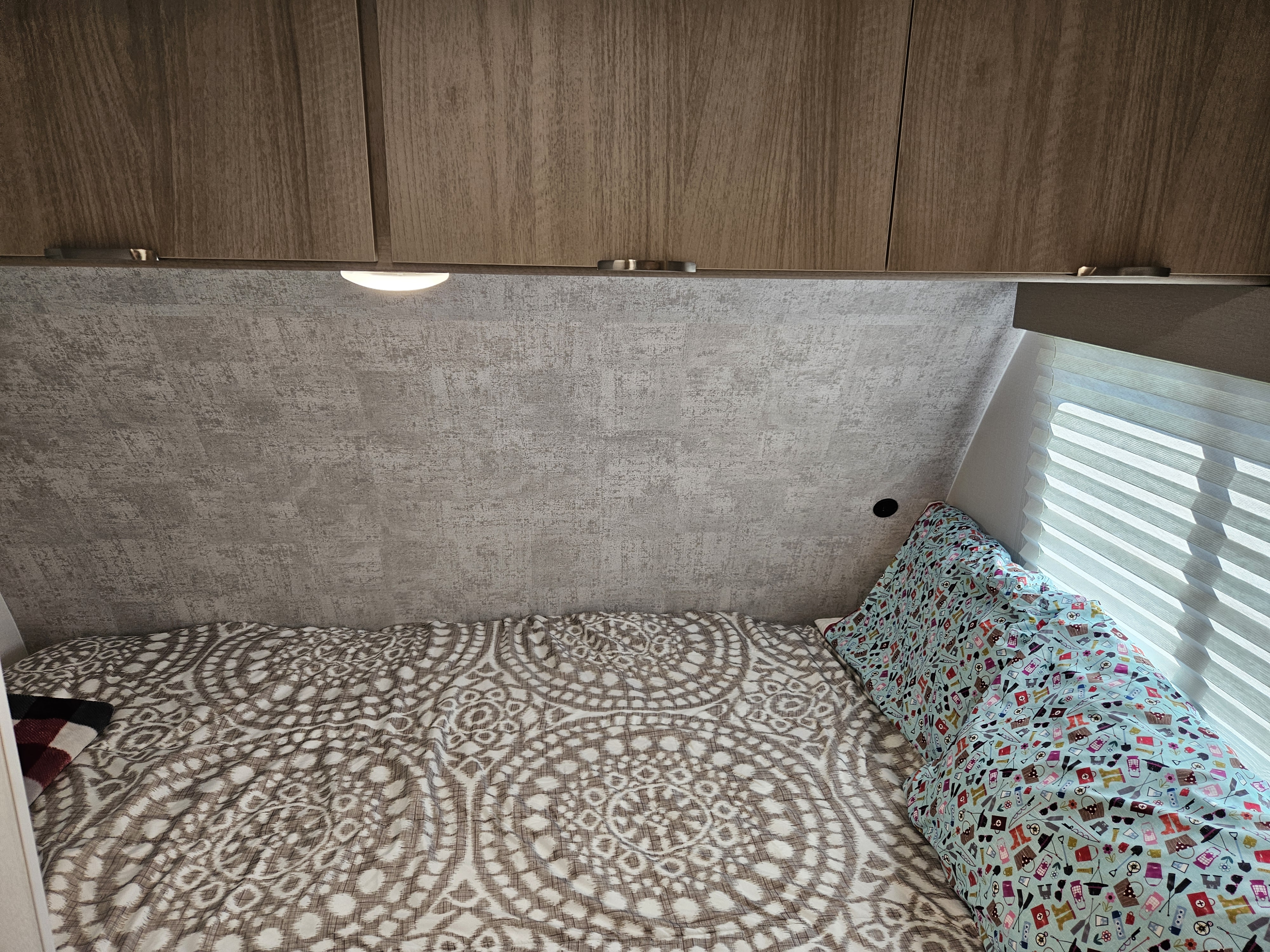 Inside an RV rental: a compact bedroom with patterned bed, overhead cabinets, and window blinds.. Winnebago Minnie Winnie 2024