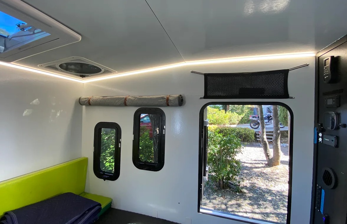 Modern RV rental interior: white walls, bright LED strip lighting, green seating, and windows with nature views.. ITWO custom Pixtech Bearlander 20 2024