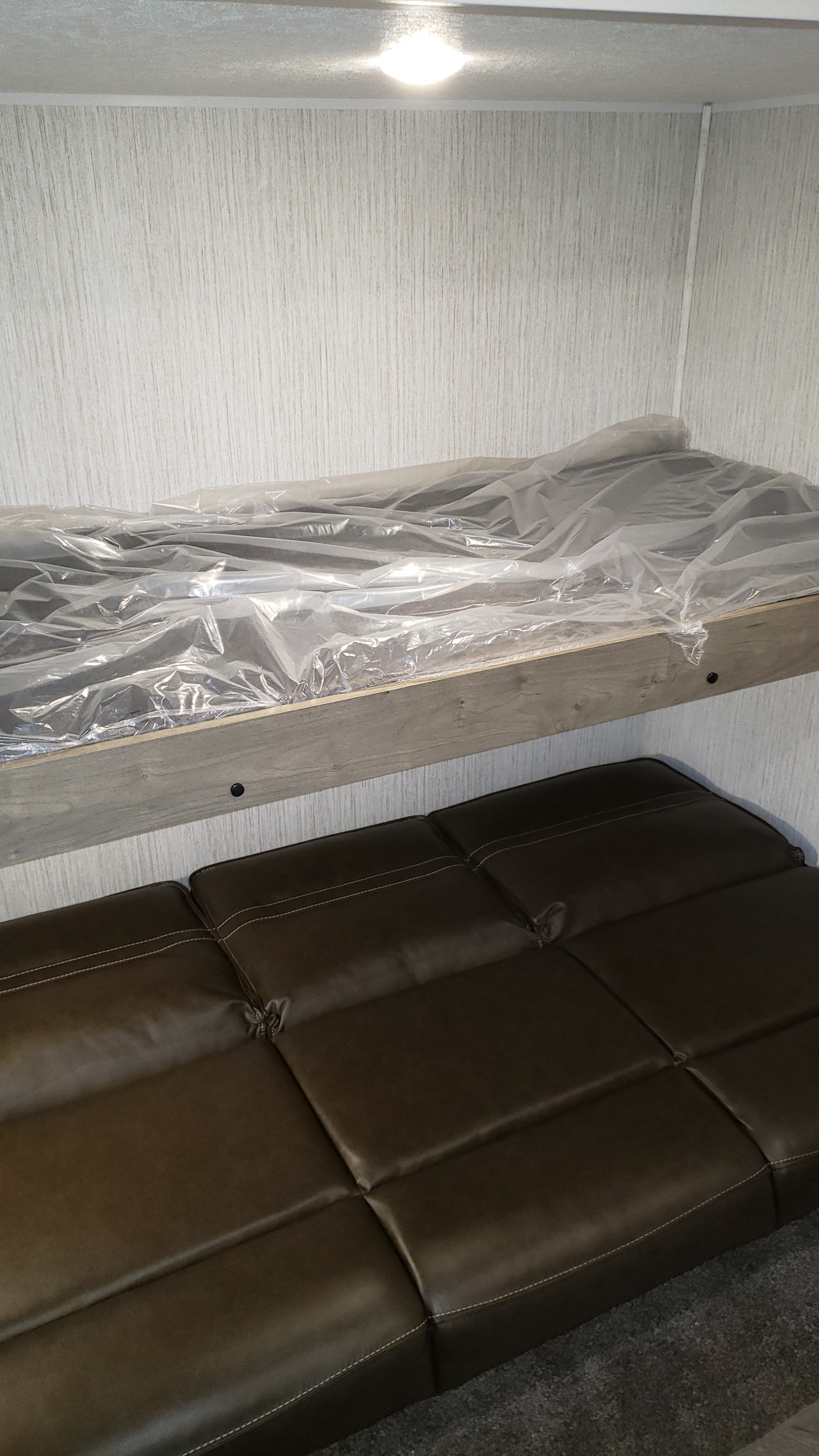 RV rental bunk beds, mattress still in plastic, and a brown sofa below. A compact, bright interior for your trip.. Palomino 32BHQS 2022