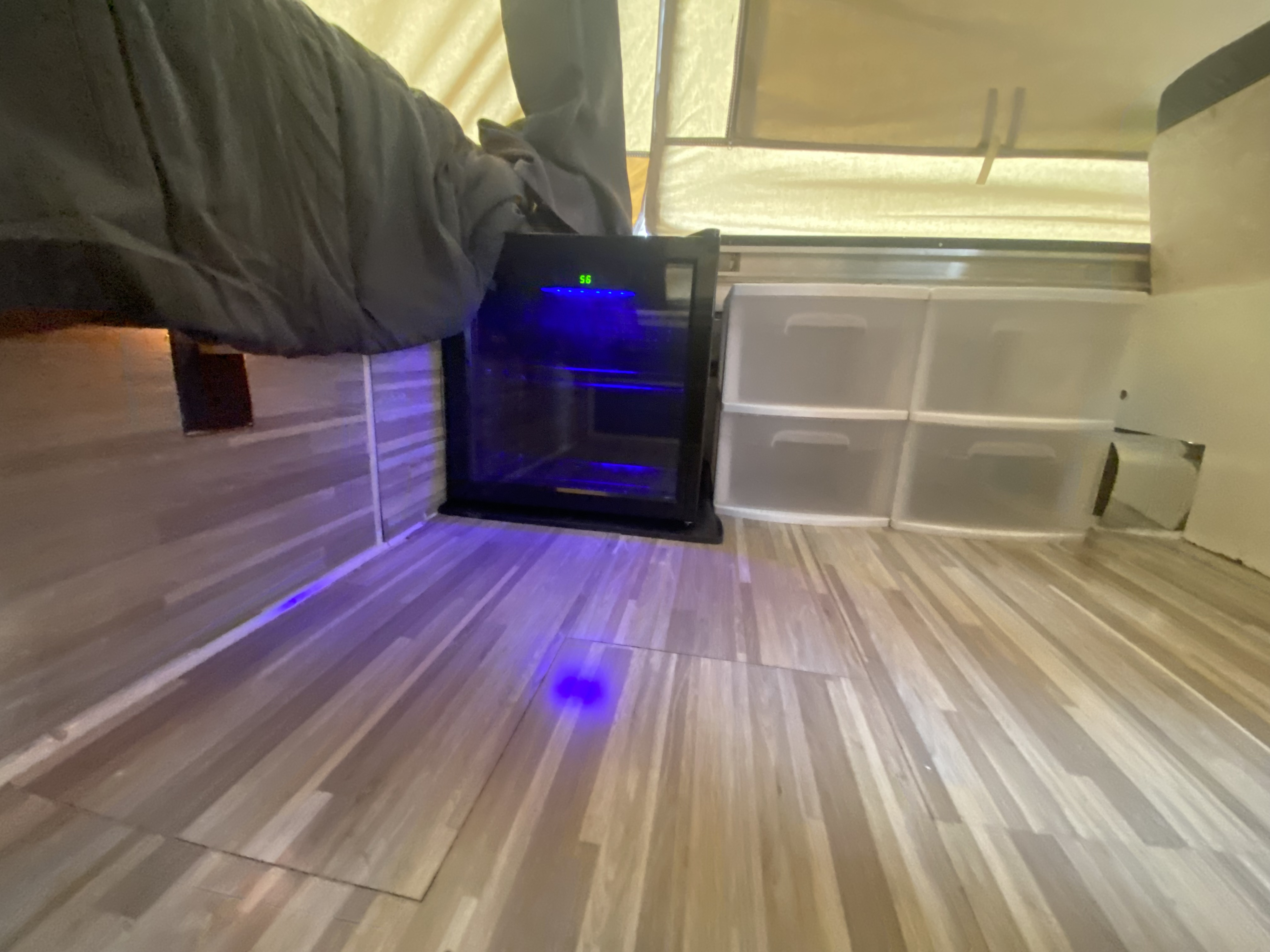 RV rental interior: cozy bed, glowing mini-fridge, and clear storage bins on wood-look flooring.. Coleman Fleetwood 1991
