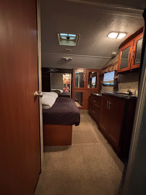 RV rental interior view: a cozy bedroom with a bed on the left, leading to a functional kitchenette with dark wood cabinets and sink on the right.. Keystone RV Fuzion Toy Hauler 2009